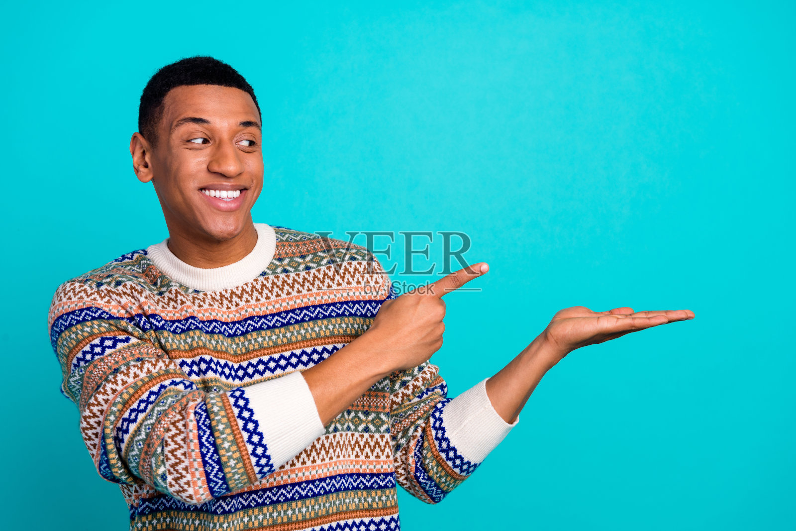 年轻男子的肖像，手指指向空白处，穿着毛衣，背景为青绿色。照片摄影图片