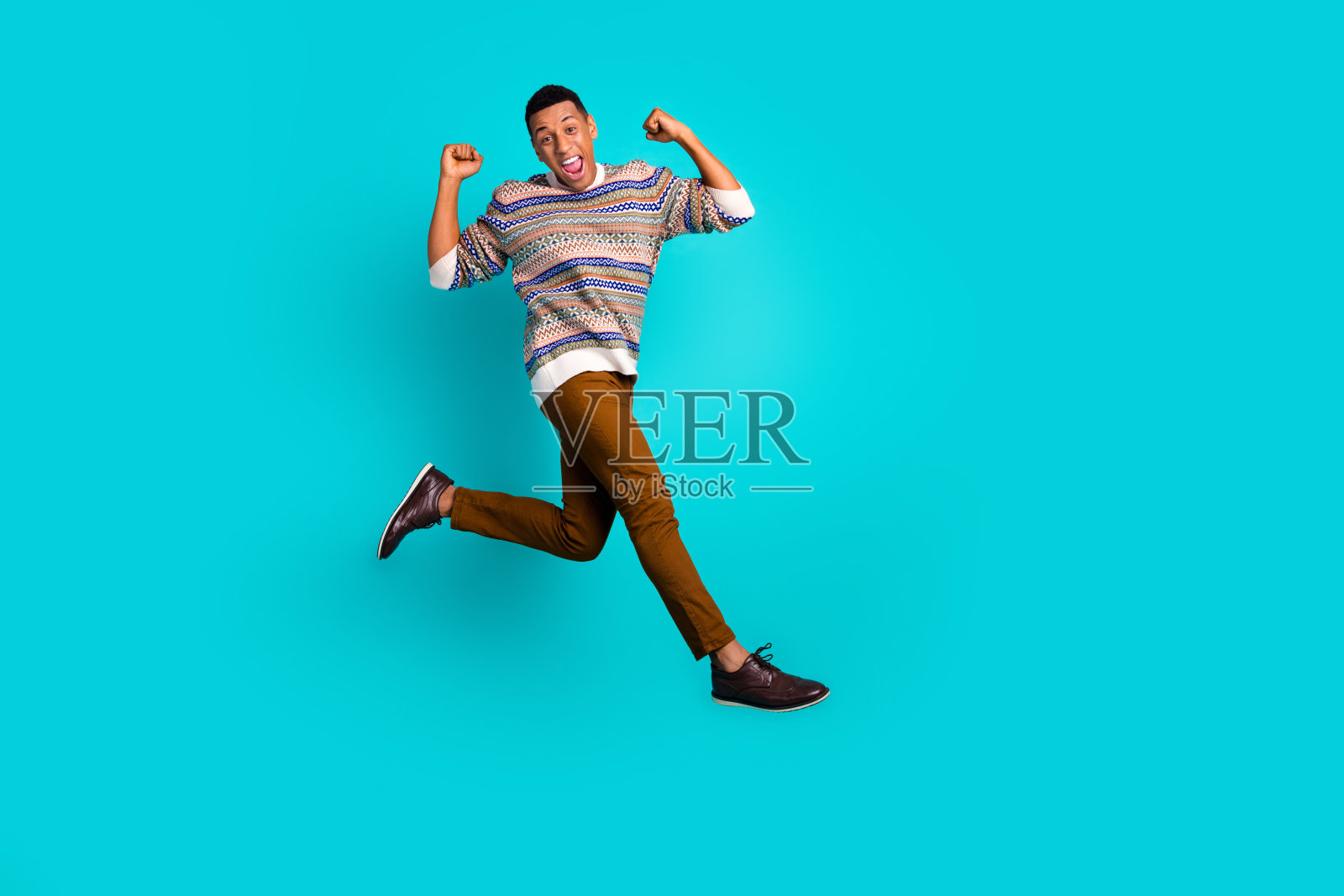 全身照：年轻帅气的男士跳起，举起拳头，穿着毛衣，背景为青绿色。照片摄影图片