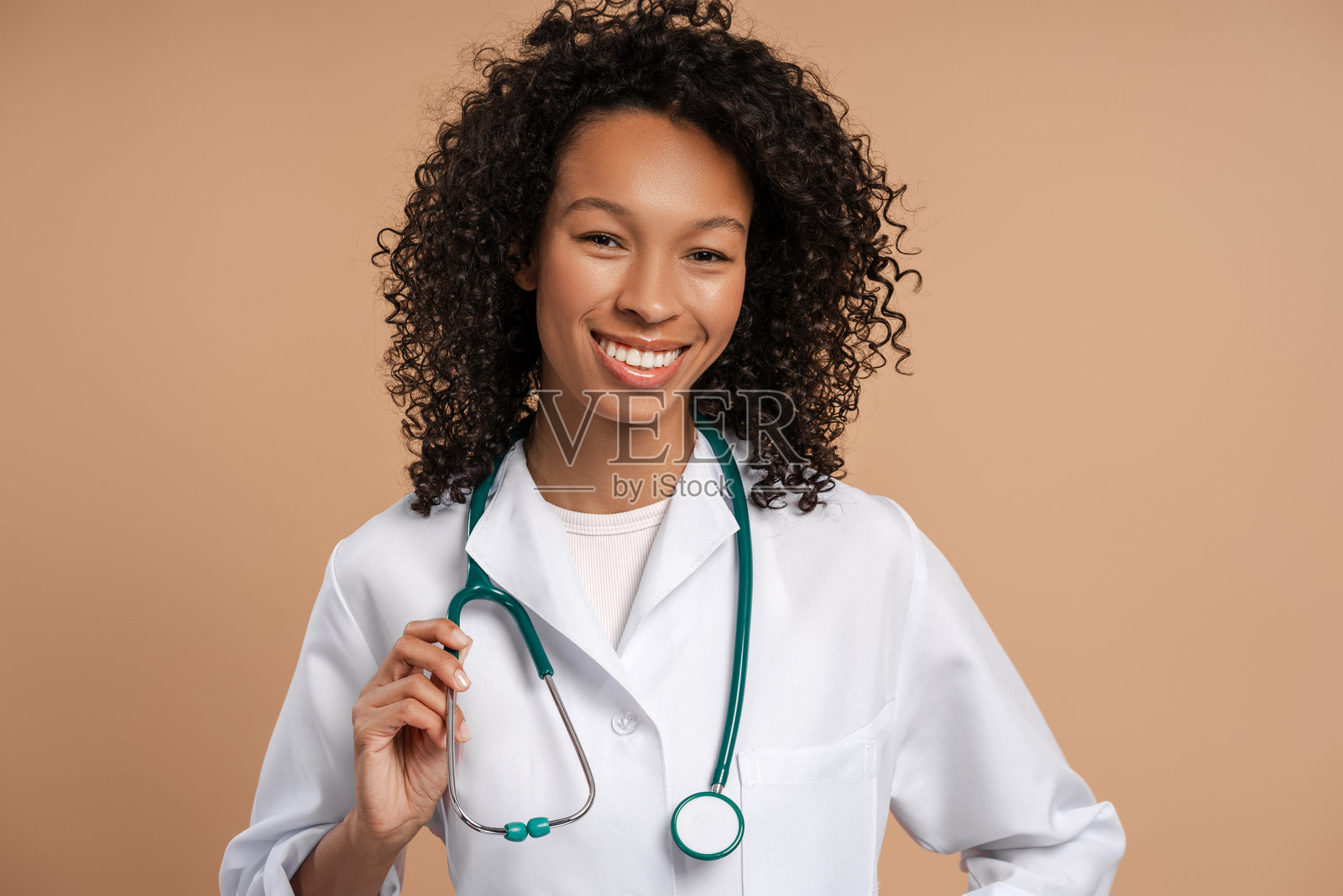 微笑的非洲女性医生穿着白大褂，佩戴听诊器，正看着镜头。照片摄影图片