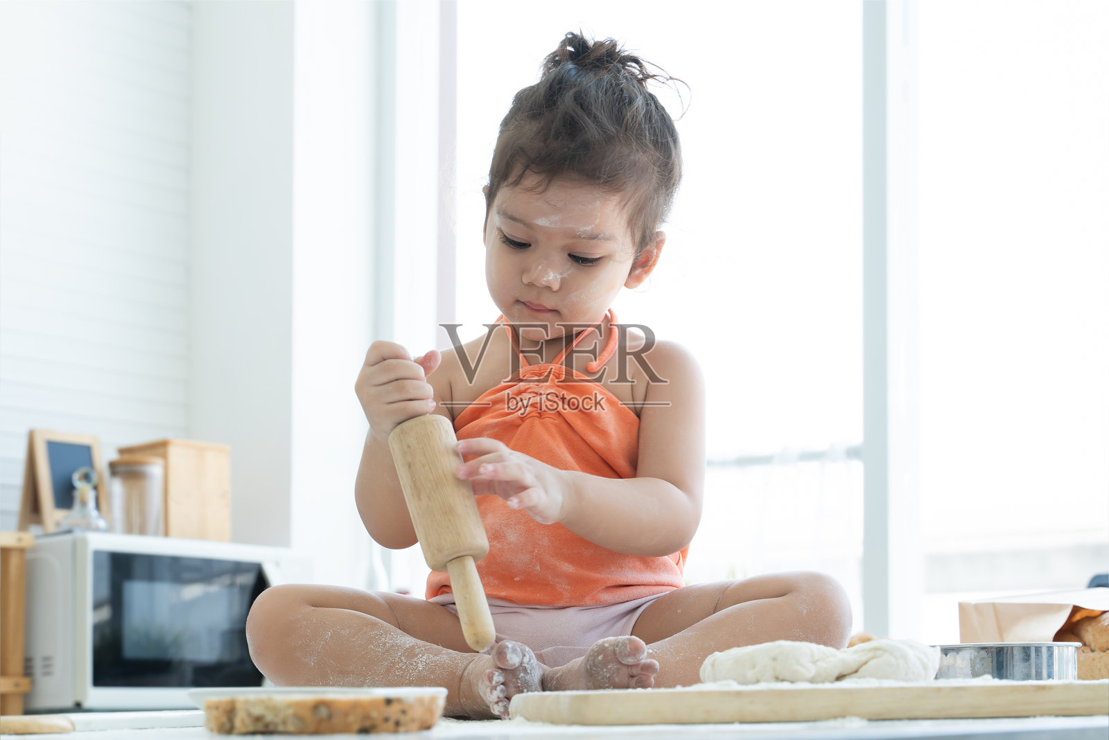 可爱的白人小女孩手持擀面杖，学习揉面和烘焙面包，坐在桌子上。孩子满身面粉，享受烹饪的乐趣，在家里的厨房里玩得很开心。照片摄影图片