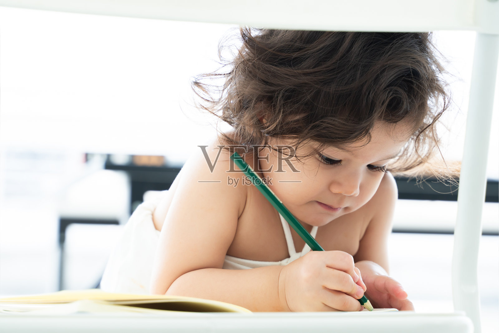 可爱的白人小女孩，卷发，正在家中用铅笔学习写字或画画，面带微笑，特写镜头。照片摄影图片