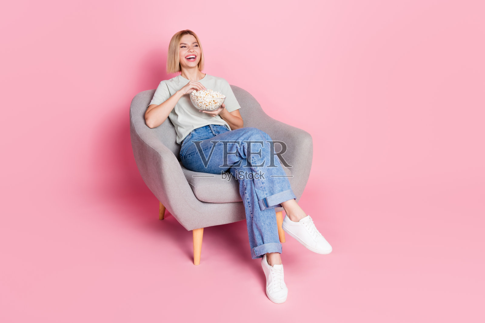 穿着时尚衣服的快乐女孩坐着享受电影，背景是粉色的空旷空间。照片摄影图片