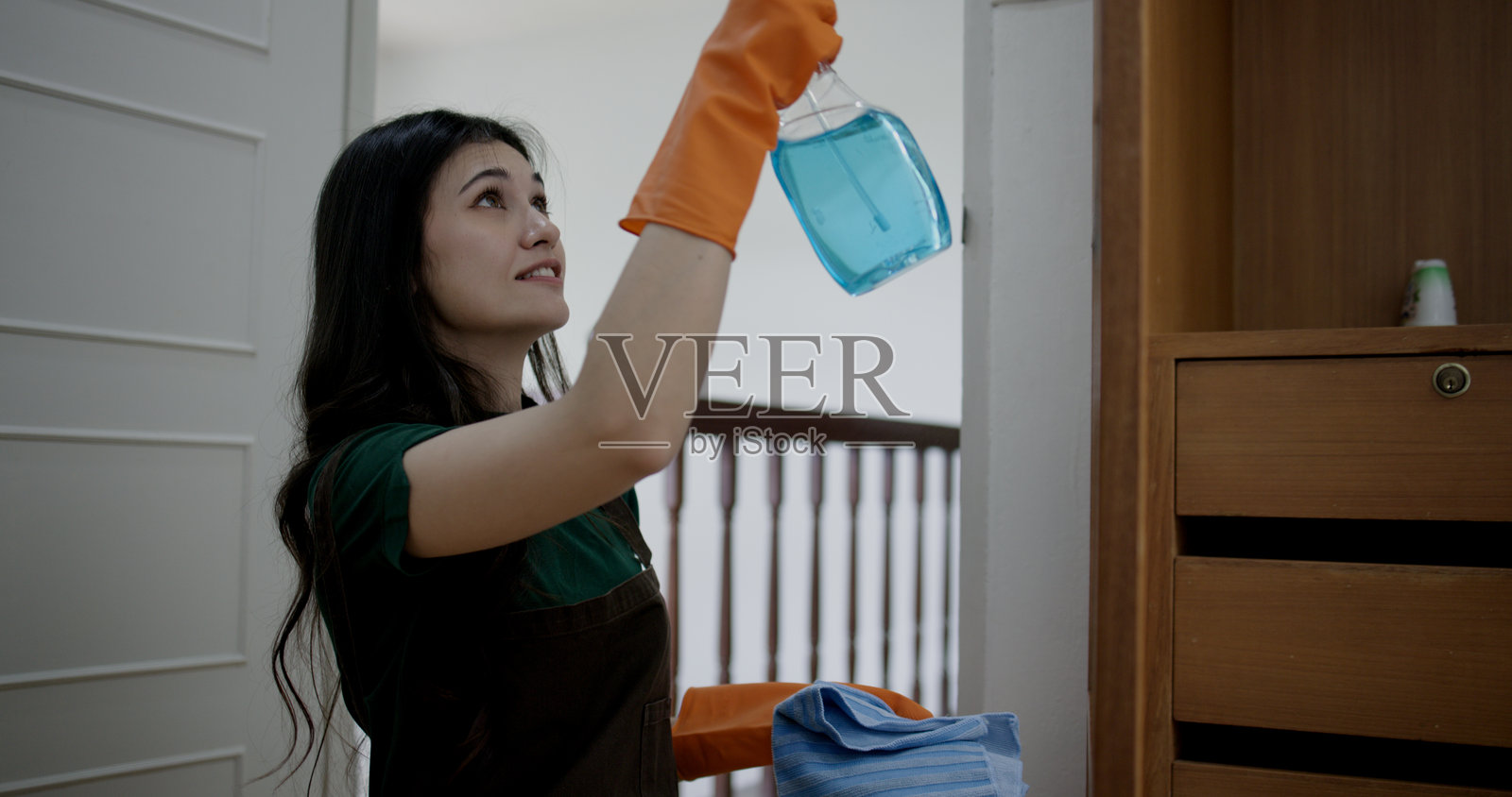 年轻女性在家卧室里用消毒湿巾和酒精喷雾清洁木质橱柜或衣柜。这突显了消毒表面以消除细菌和病毒的重要性。照片摄影图片