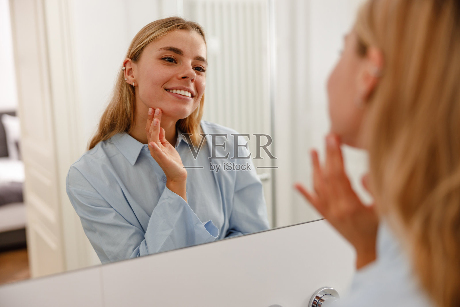 一位女性愉快地享受她的护肤程序，同时对着镜子微笑。照片摄影图片