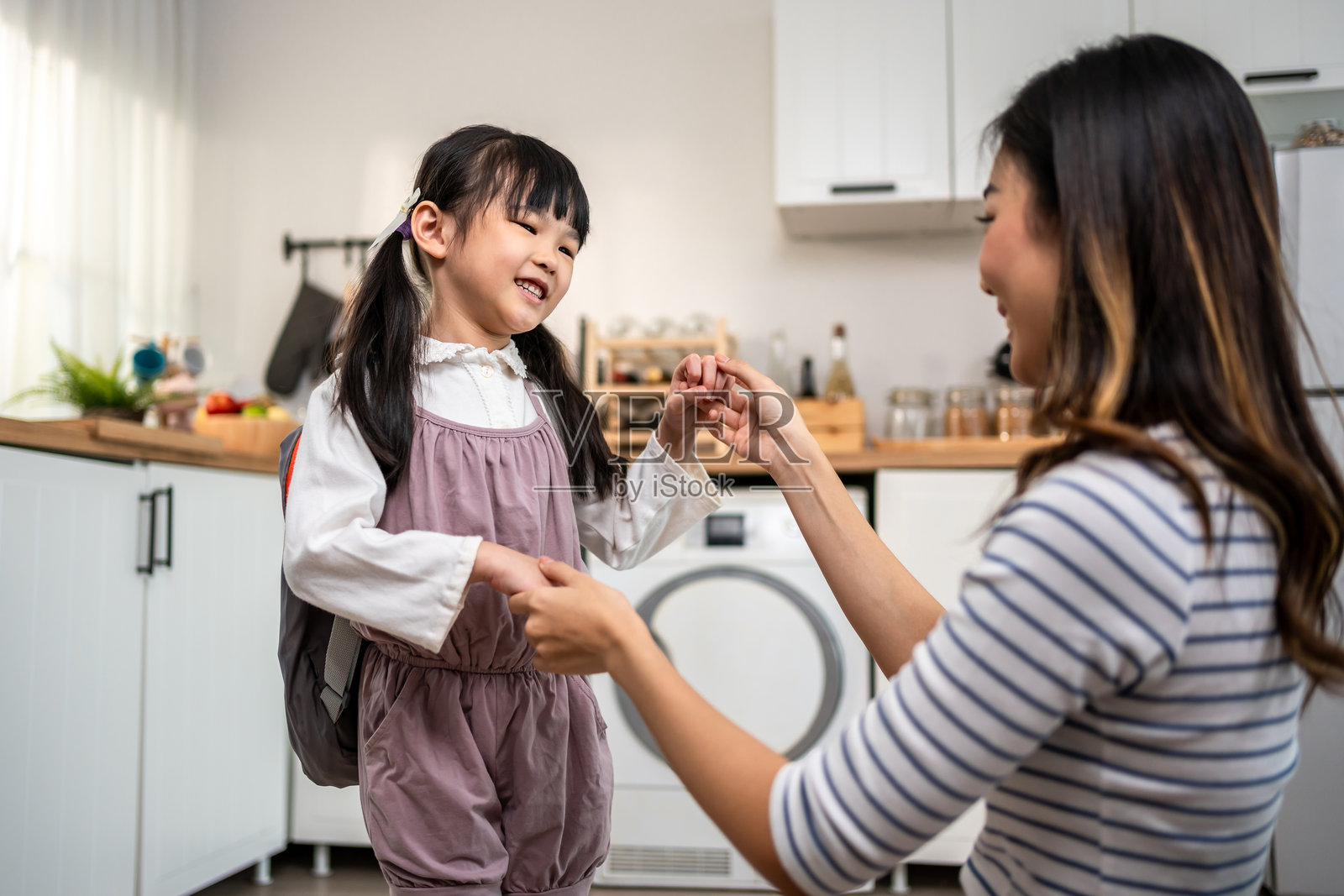 亚洲美丽的母亲在家为年轻女儿准备上学的背包。可爱的女孩在准备时感到快乐和兴奋，期待着假期后与妈妈一起回到幼儿园的第一天。照片摄影图片