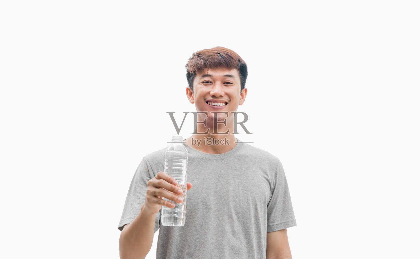 一位穿着灰色T恤的帅气亚洲男子，手持水瓶，面带快乐自信的微笑，背景为灰色。健康饮水的概念，暗示水的好处。照片摄影图片