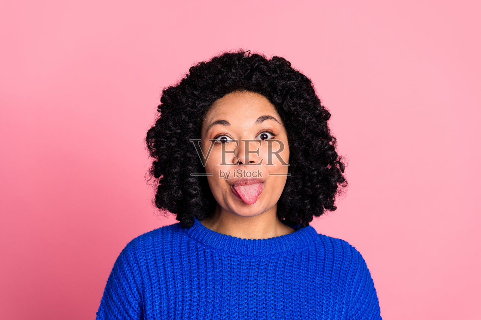 穿着蓝色针织时尚服装的愉快可爱女性肖像，背景为粉色。照片摄影图片