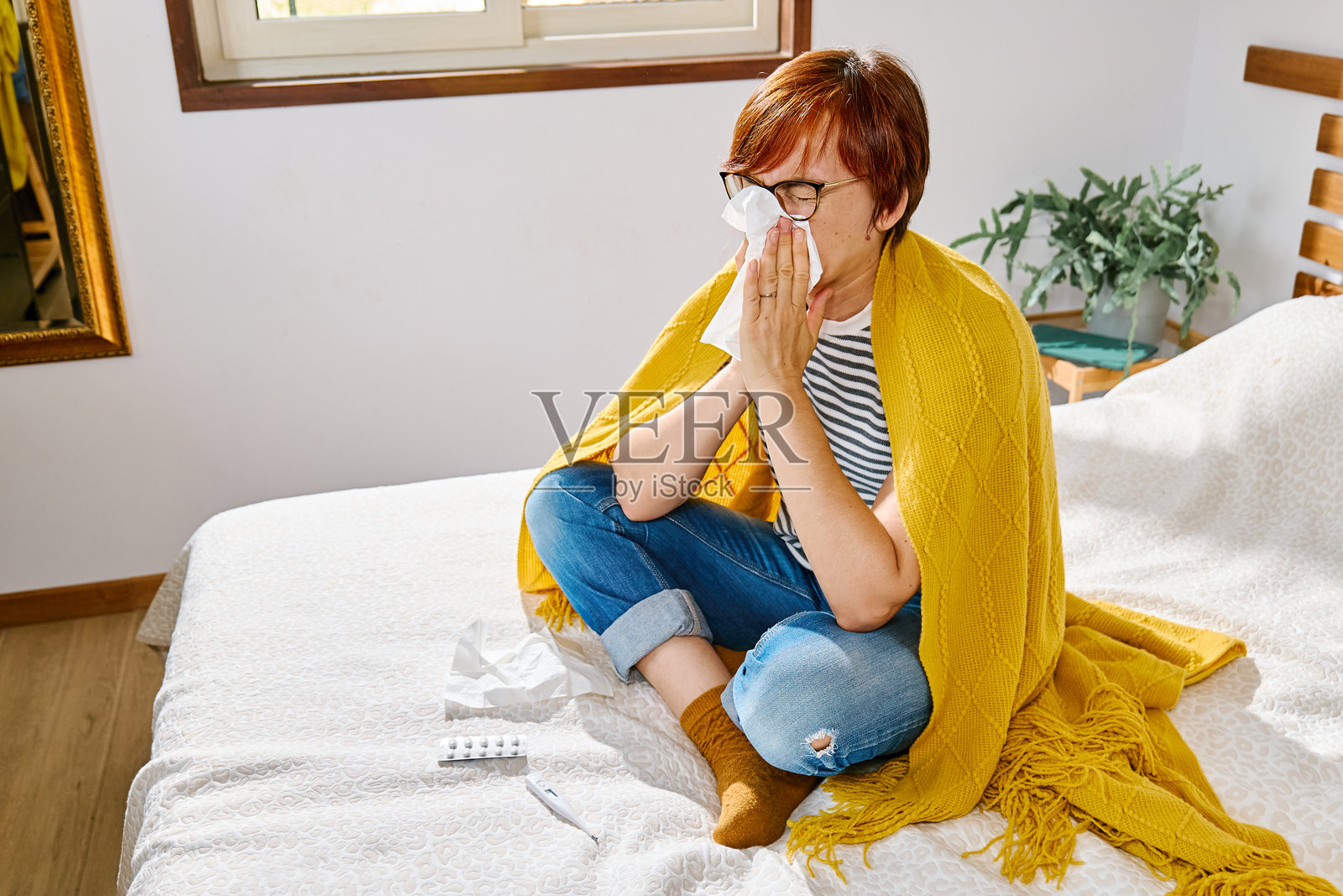 生病的女人坐在床上用面巾纸擤鼻子。照片摄影图片