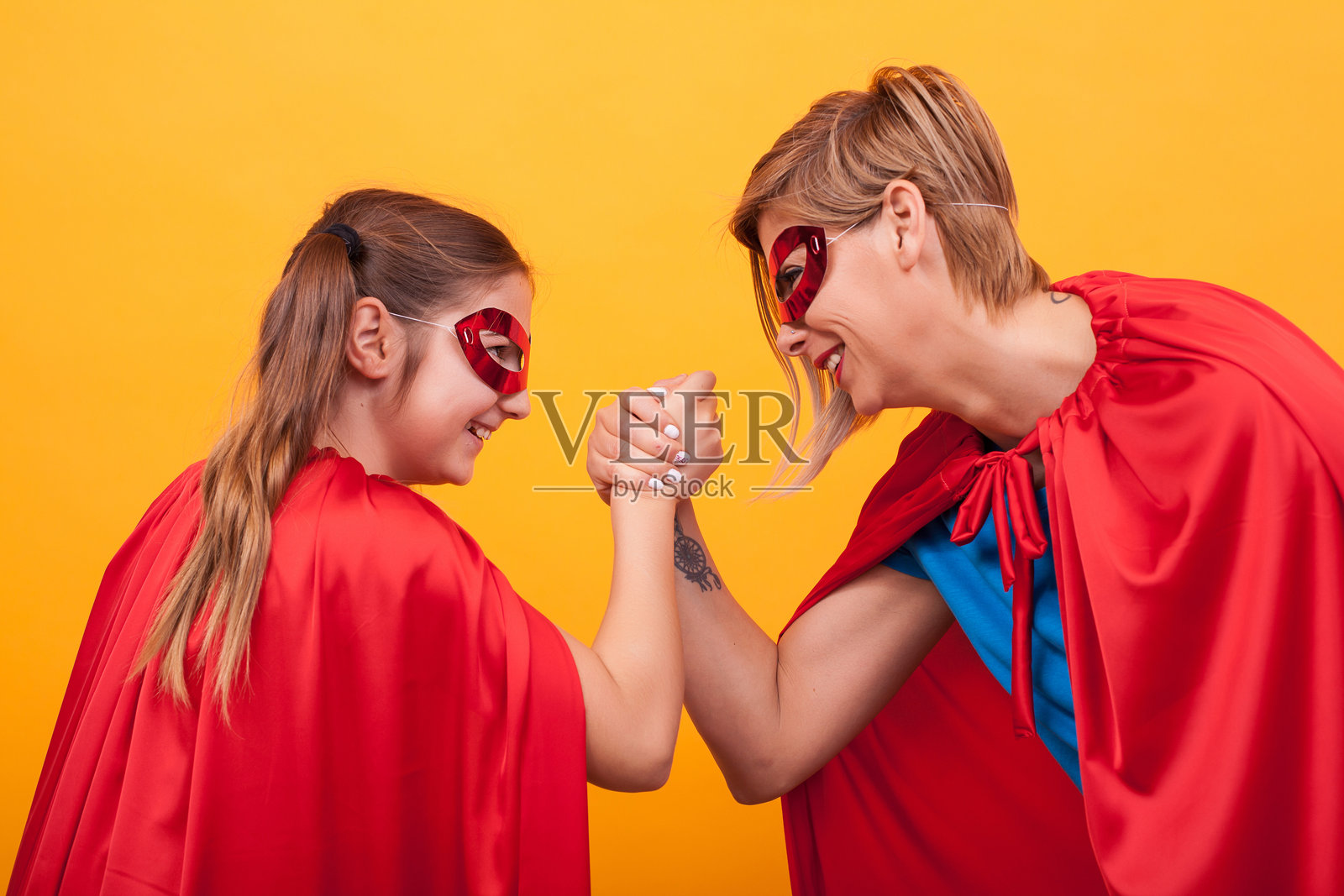 母女俩打扮成超级英雄，在黄色背景下进行摔跤比赛。照片摄影图片