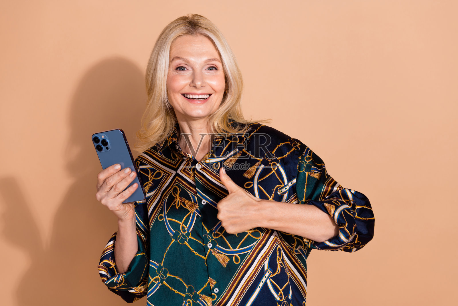 成熟金发女商人在米色背景下穿着时尚衬衫，使用手机的肖像照片照片摄影图片