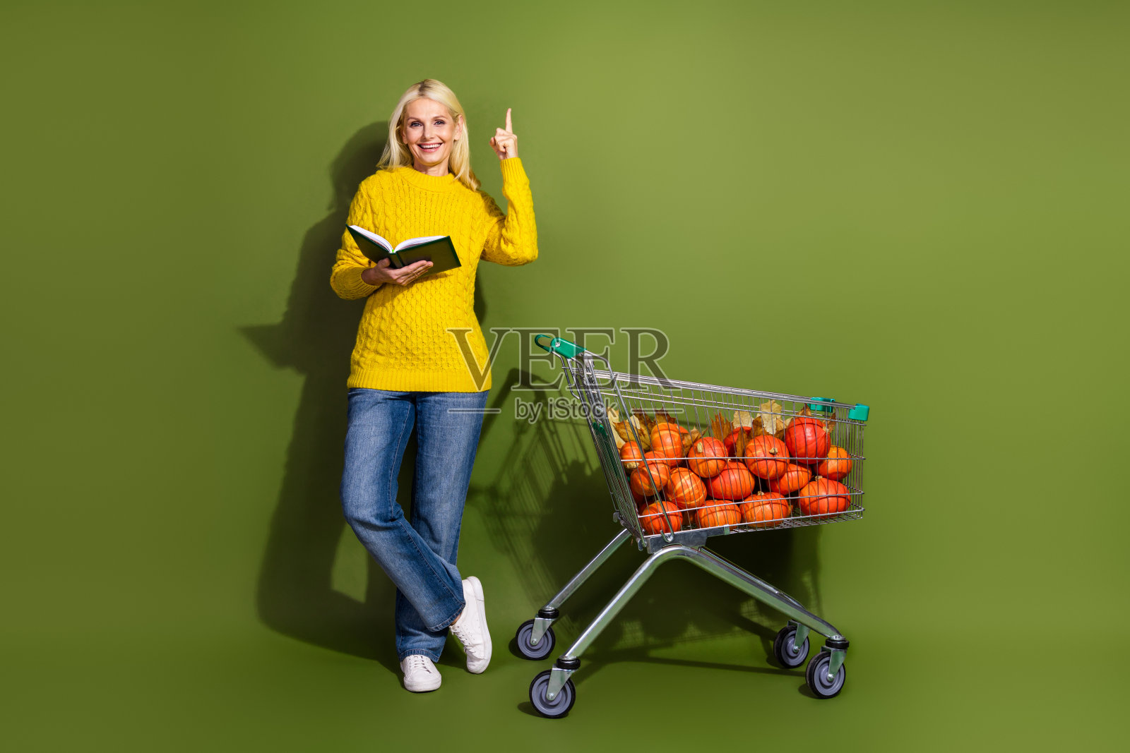 快乐可爱的退休老人推着购物车，手持计划本，空白空间，背景为绿色。照片摄影图片