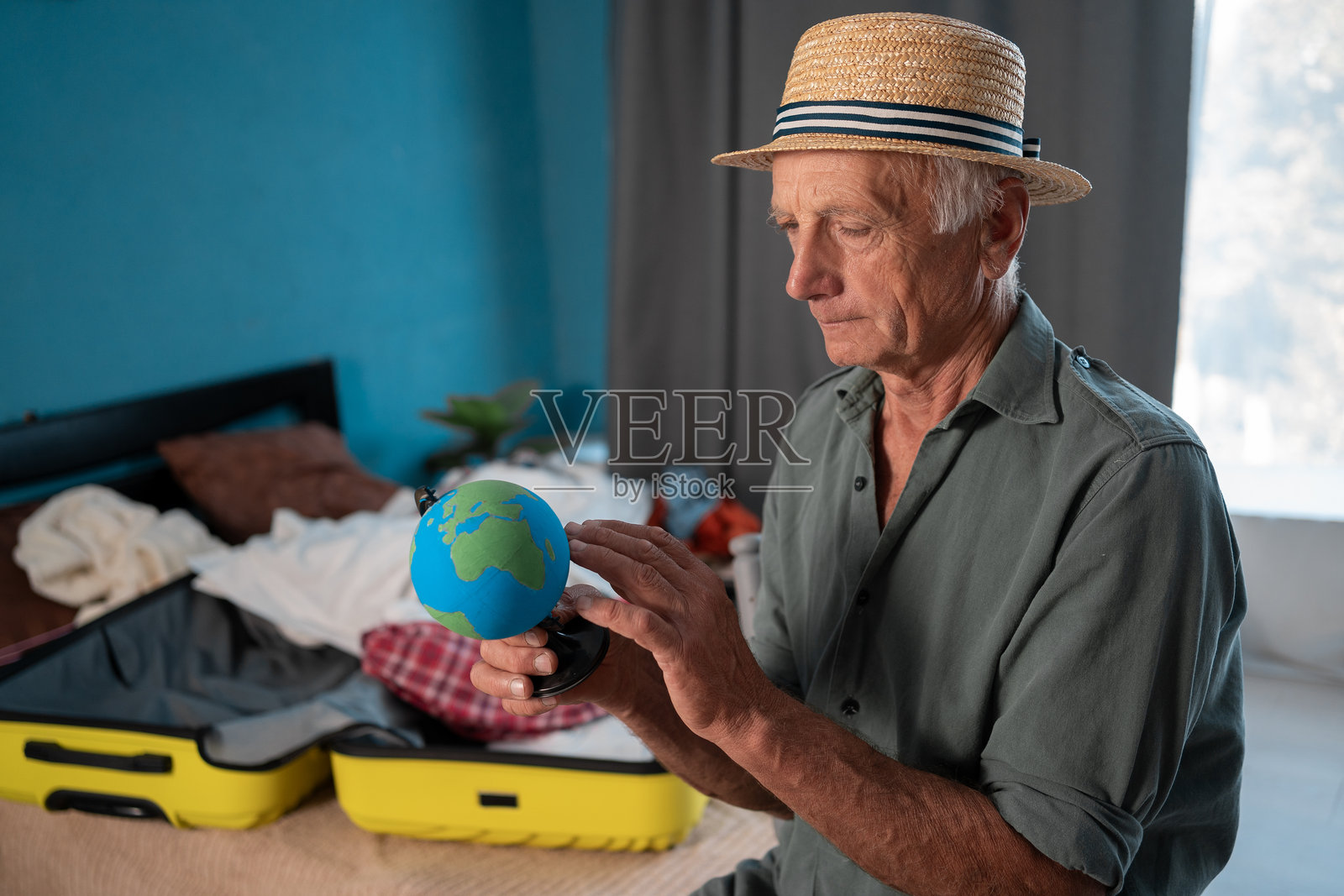 老人准备旅行，坐在家中选择地球仪上的国家，为退休后的假期做准备照片摄影图片