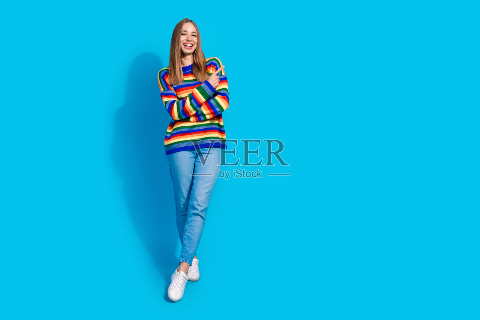 可爱的积极女孩穿着条纹彩色衣服，推荐在蓝色背景上留白空间。照片摄影图片