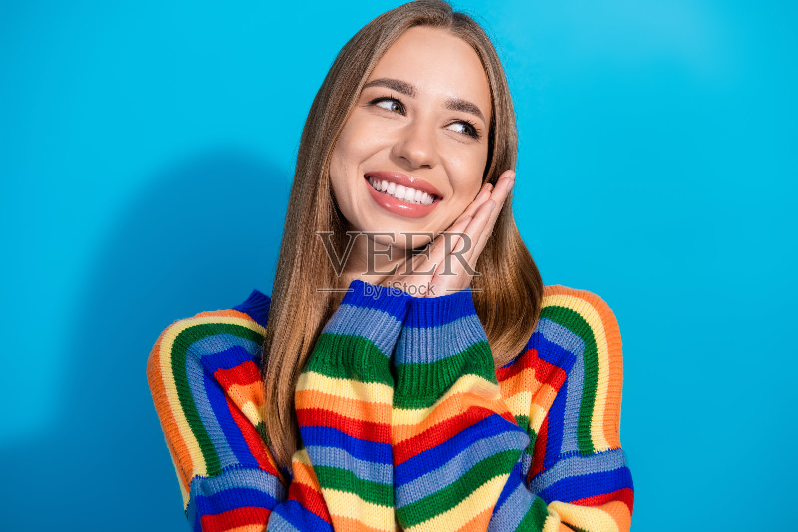 可爱的漂亮女孩穿着条纹彩色衣服，手臂托着脸颊，背景为空旷的蓝色。照片摄影图片