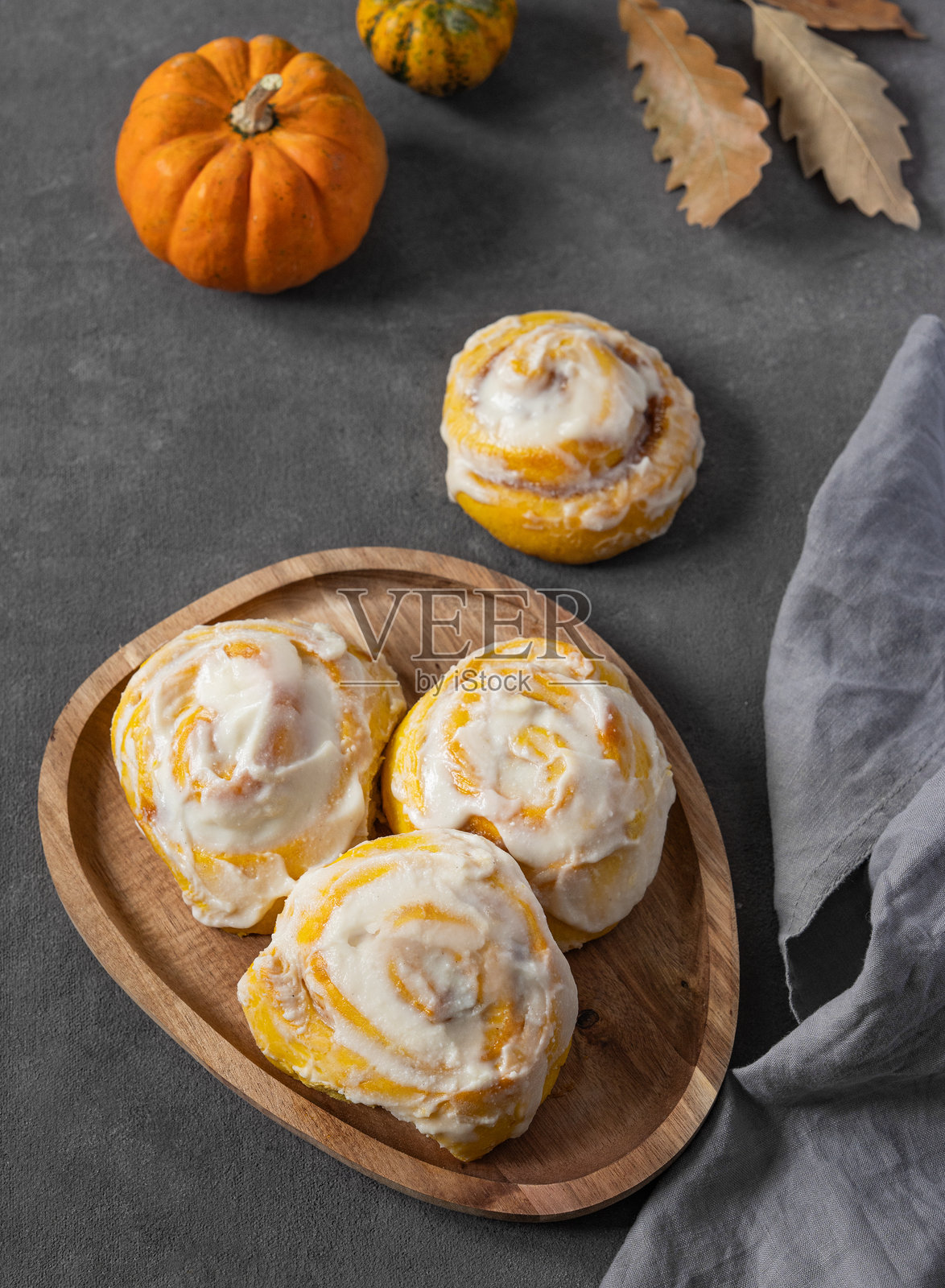 木盘上放着南瓜卷，淋上奶油糖霜和肉桂，背景为深色，旁边有餐巾。照片摄影图片