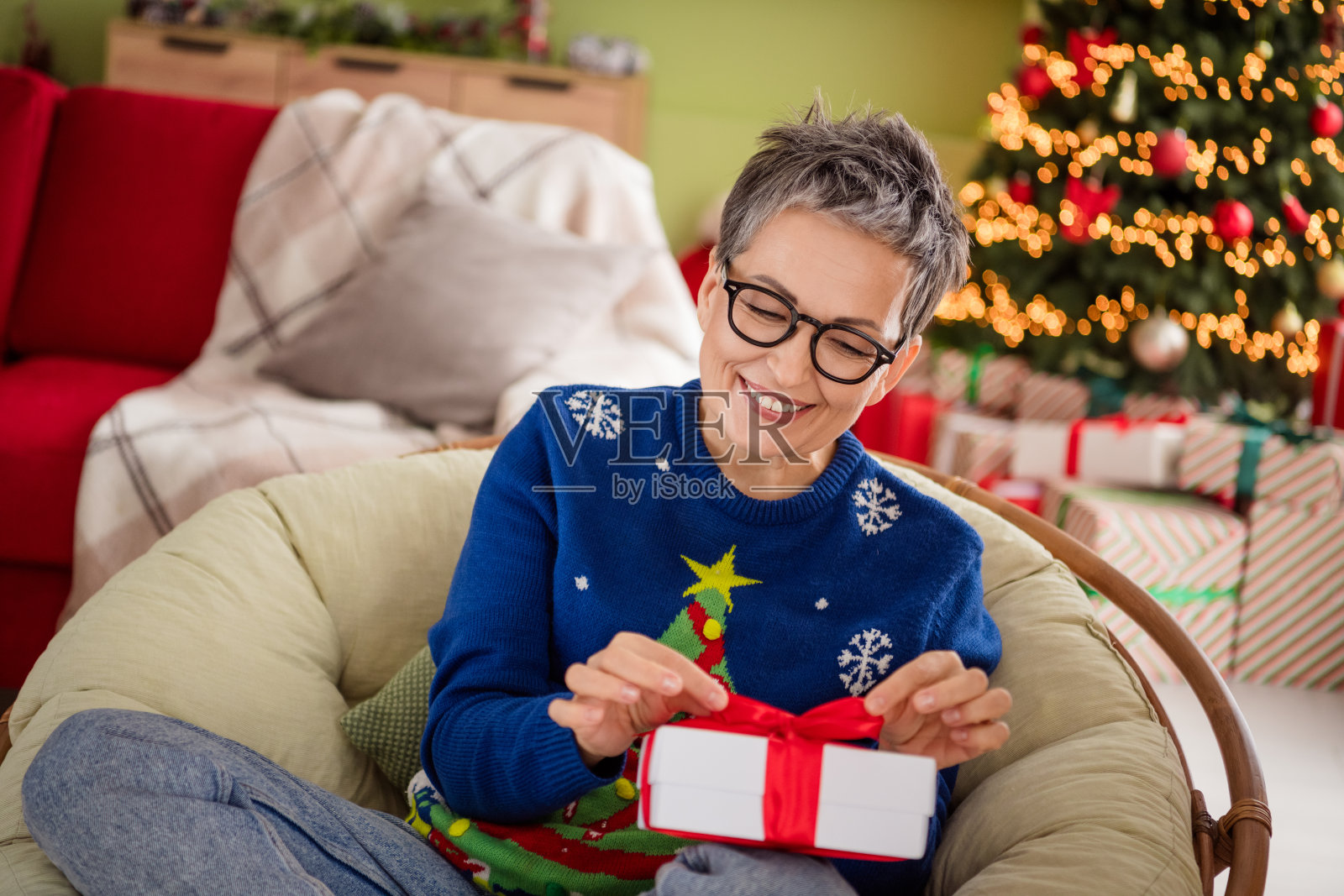 可爱的快乐女性穿着蓝色毛衣，在室内庆祝圣诞奇迹，打开礼物的氛围照片摄影图片