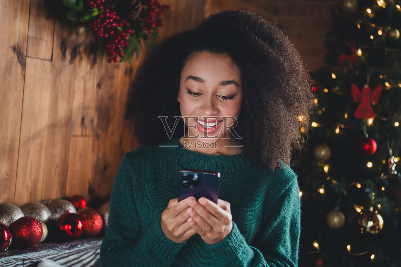 年轻女孩在室内穿着毛衣，使用智能手机发短信，庆祝新年和圣诞节。照片摄影图片