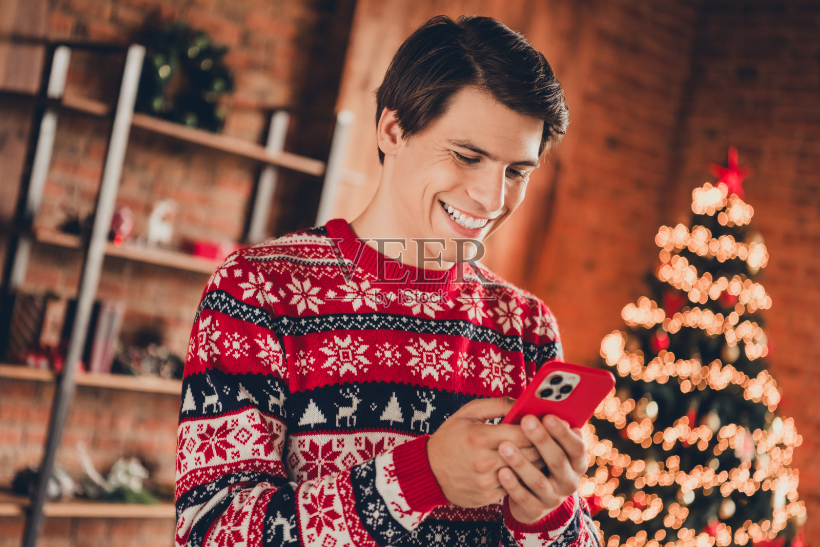 穿着印花毛衣的迷人搞笑男士在室内家中庆祝圣诞节，使用现代设备聊天照片摄影图片
