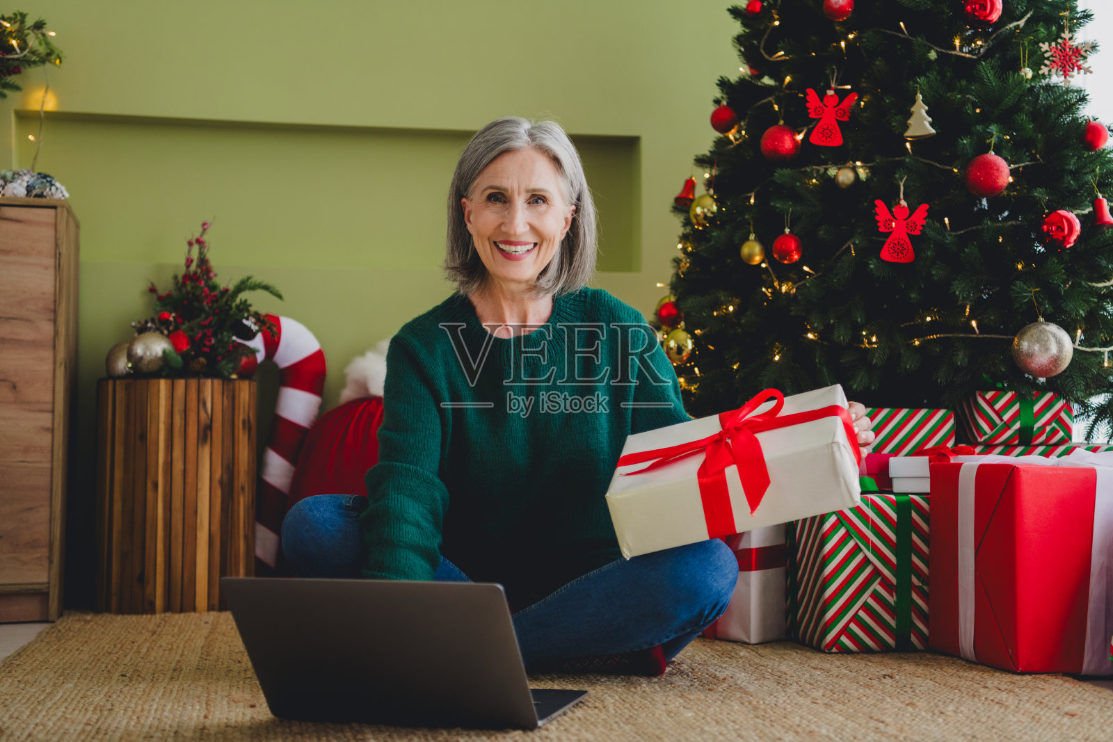可爱的女人坐在地板上，穿着绿色毛衣，享受新年和圣诞节的室内氛围，准备购买礼物。照片摄影图片