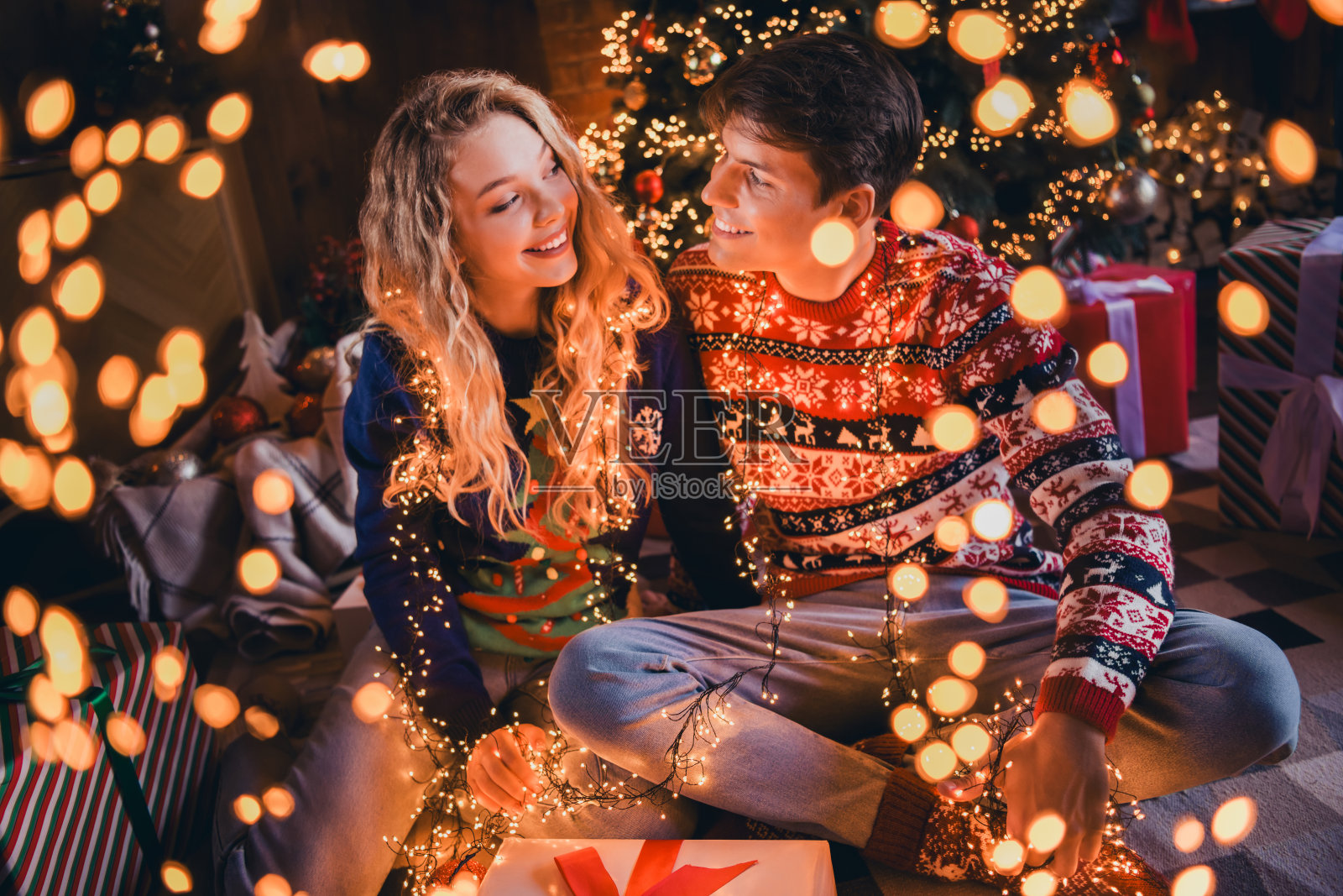 一对年轻情侣全身照，互相凝视，穿着圣诞服装，享受温馨的圣诞派对装饰，室内公寓环境。照片摄影图片