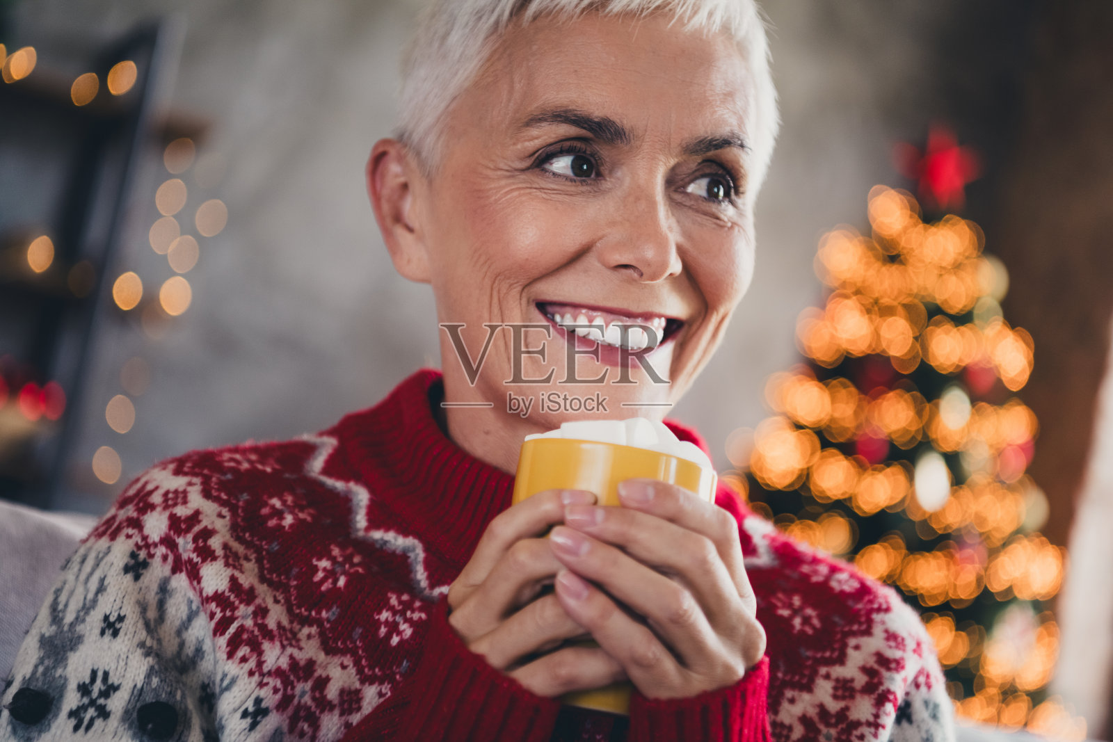 一位可爱的年长女性在室内公寓中手持棉花糖蛋奶酒杯，思考着圣诞节的节日氛围。照片摄影图片