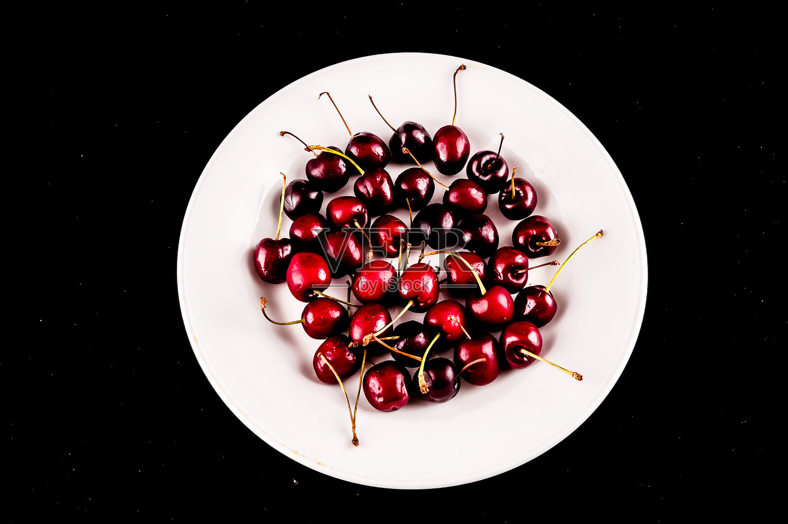 一盘樱桃放在黑色背景上照片摄影图片