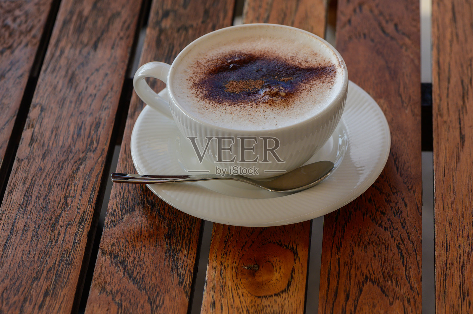 一杯温暖的泡沫咖啡静静地放在木桌上，邀请着温馨的对话和愉快的时光，在阳光明媚的午后。照片摄影图片