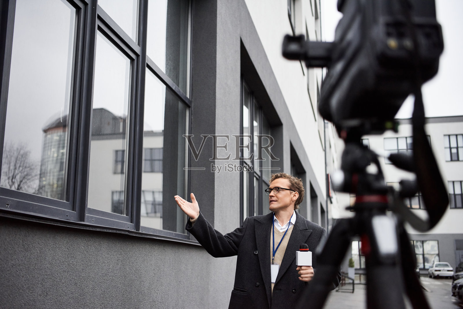 一位戴眼镜的记者在现代建筑外激情地报道新闻，天空阴云密布。照片摄影图片