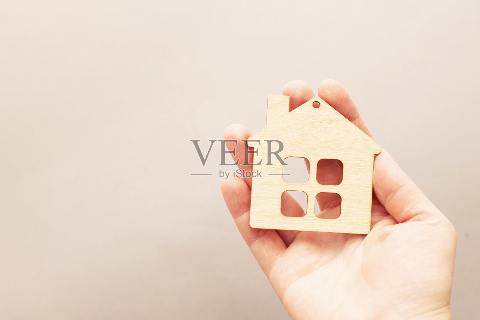 人手握着一个木制玩具房子，背景为米色。这与购房或家庭心理学有关。照片摄影图片