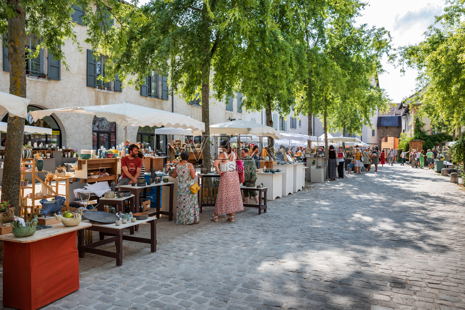 克雷米厄小镇树下的户外陶艺和陶瓷市场，游客们在参观。照片摄影图片