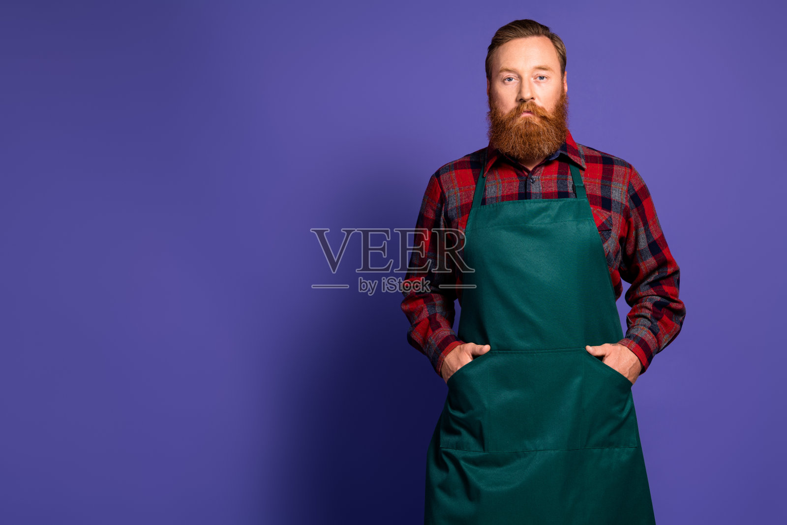 时尚的农夫穿着红色格子衬衫和绿色围裙，站在紫色背景的空旷空间中。照片摄影图片