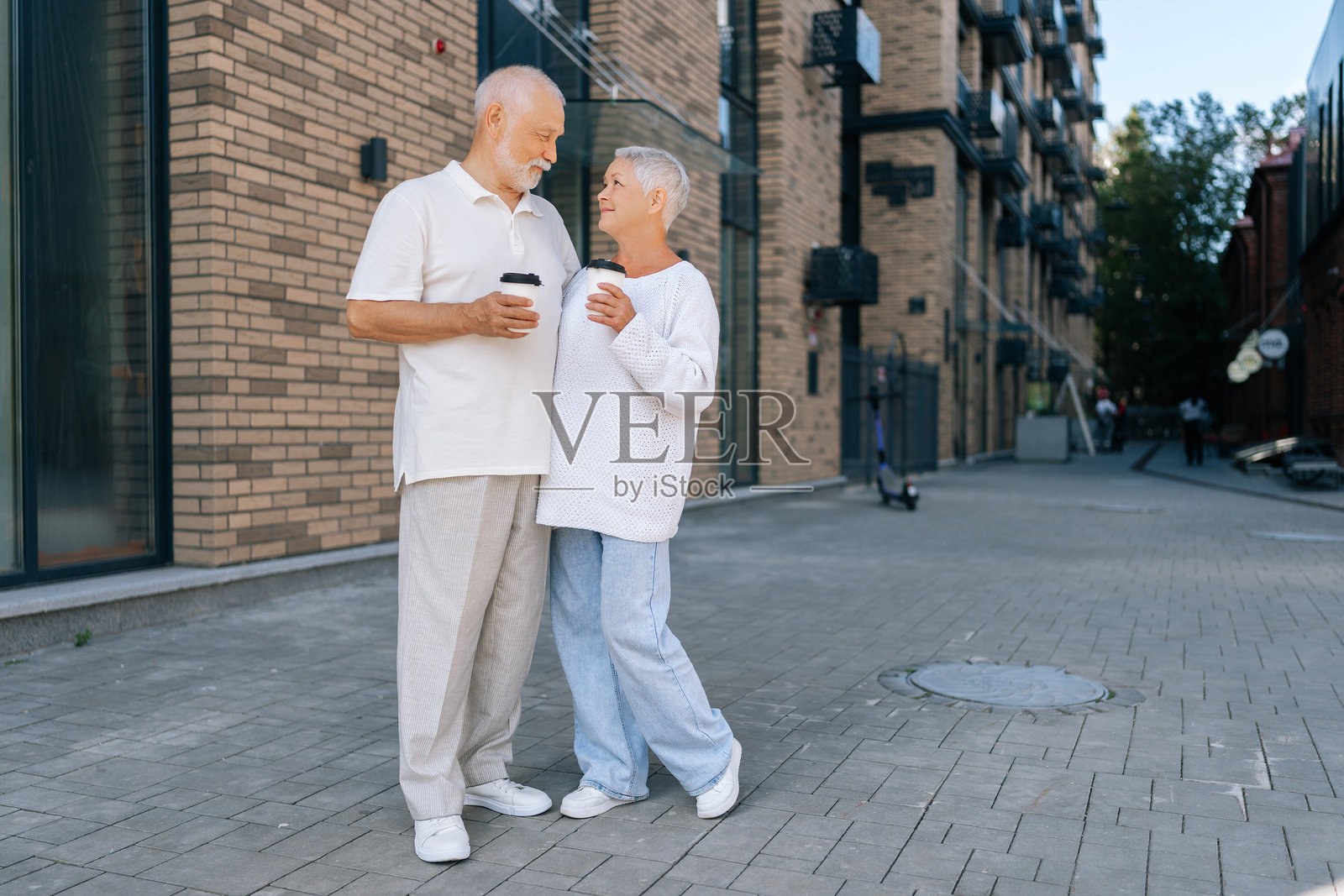 一对恩爱老年夫妇在城市街道上享受咖啡，微笑交谈，享受阳光下的亲密时光。照片摄影图片