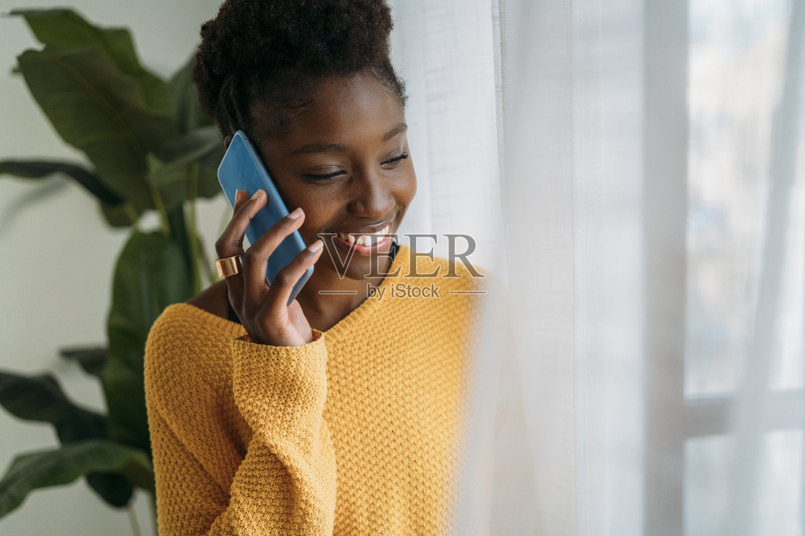 一位愉快的女性在窗边打电话，微笑着，身处温馨的日光环境中照片摄影图片