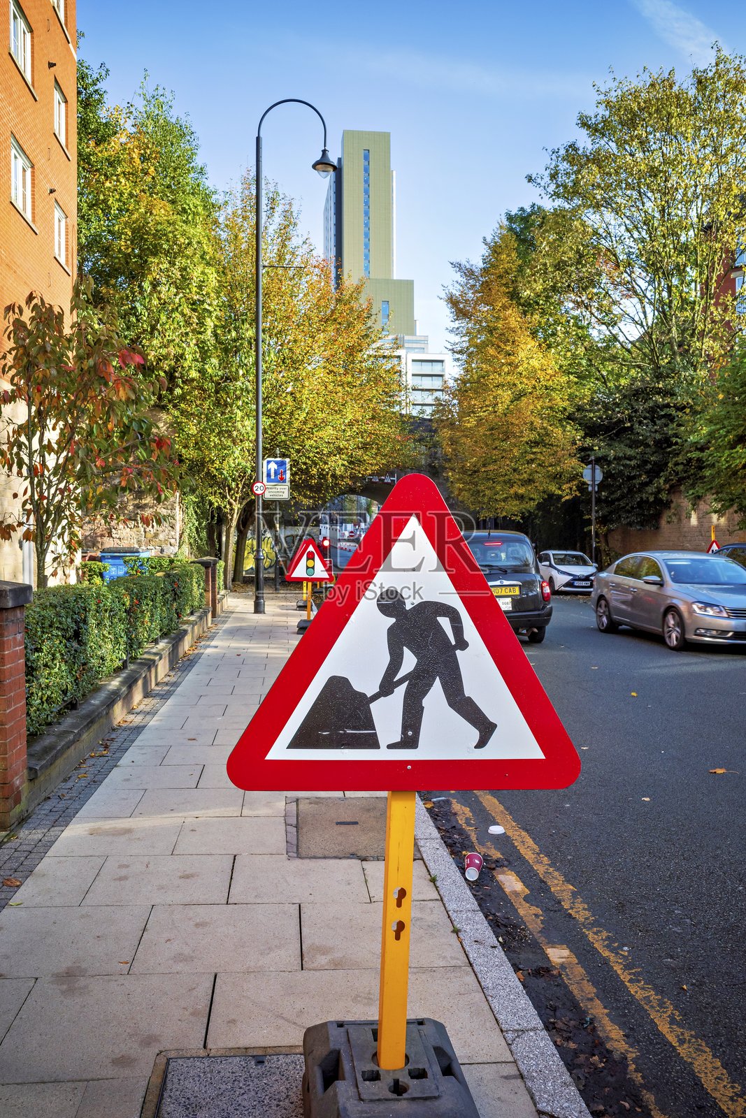 城市街道上的道路施工标志，背景是秋天的树木和汽车。照片摄影图片
