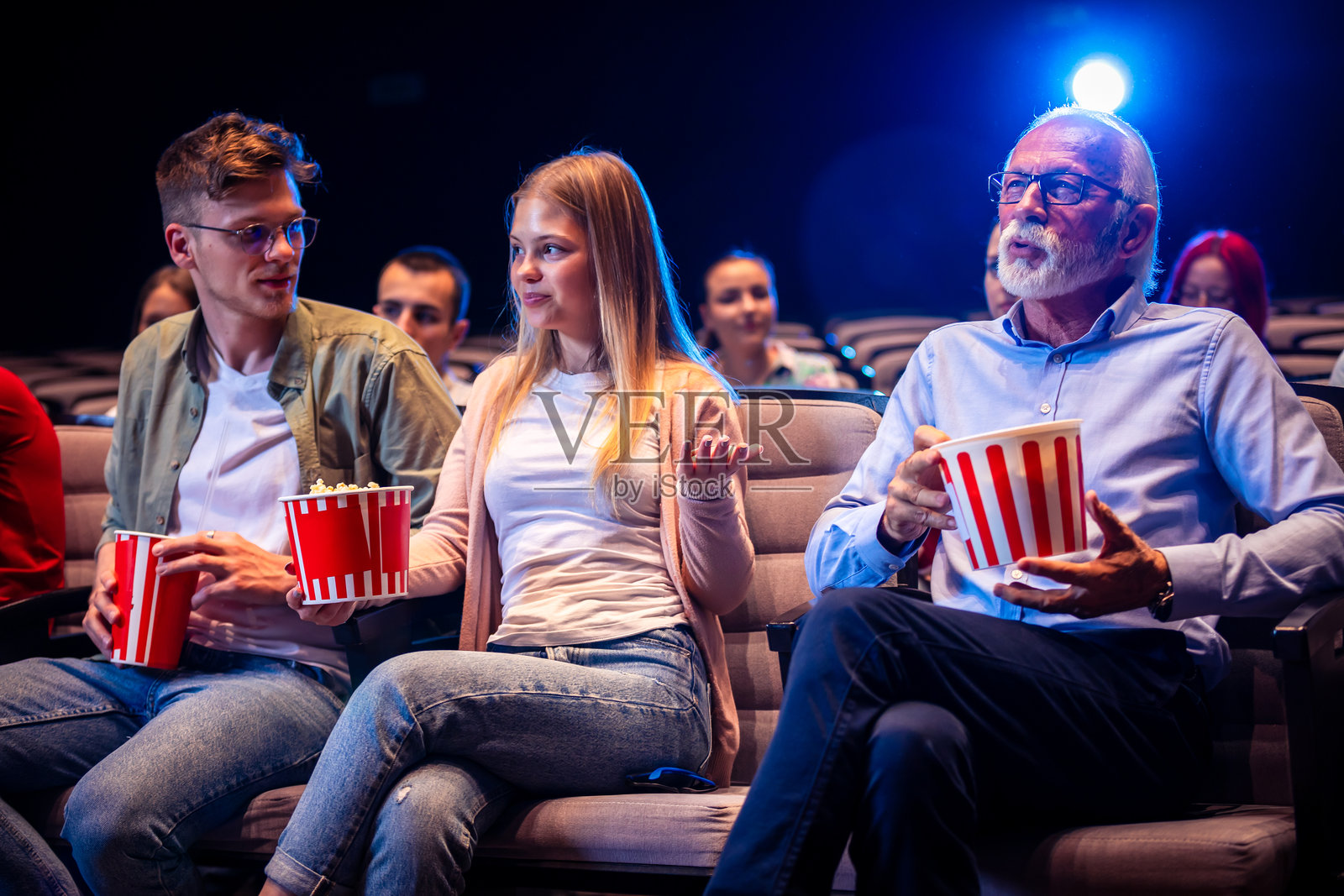 一群人在电影院观看电影，他们吃着爆米花，喝着果汁。照片摄影图片