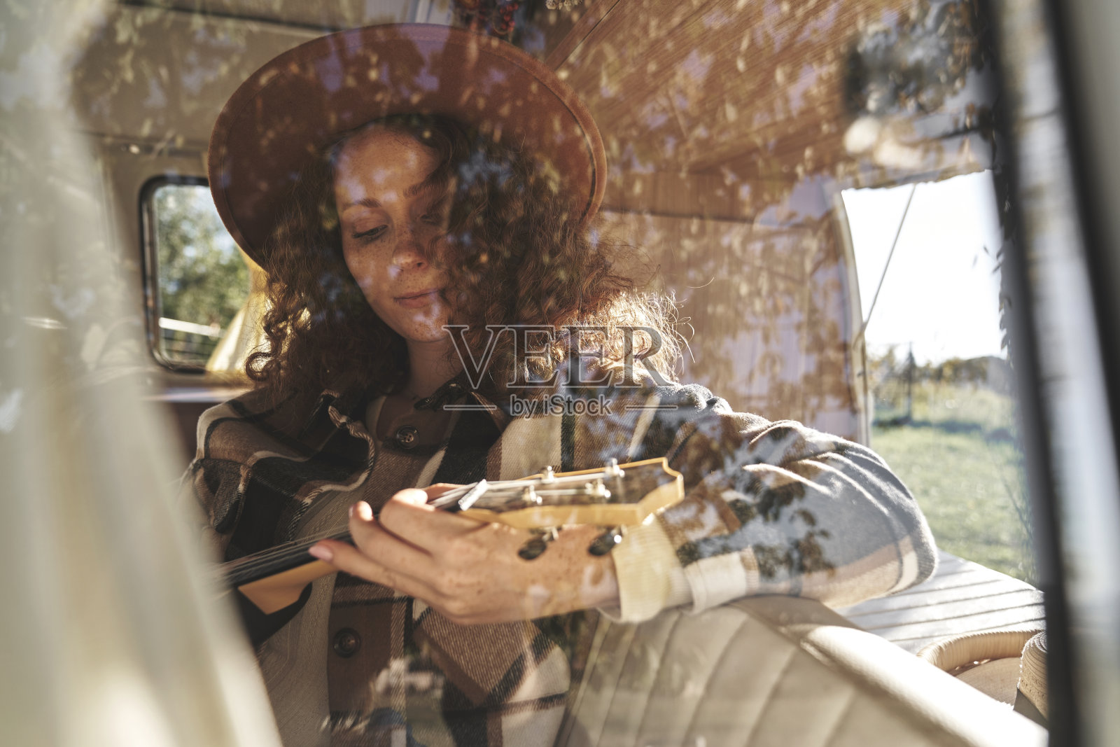在复古露营车内弹奏尤克里里的小女人照片摄影图片