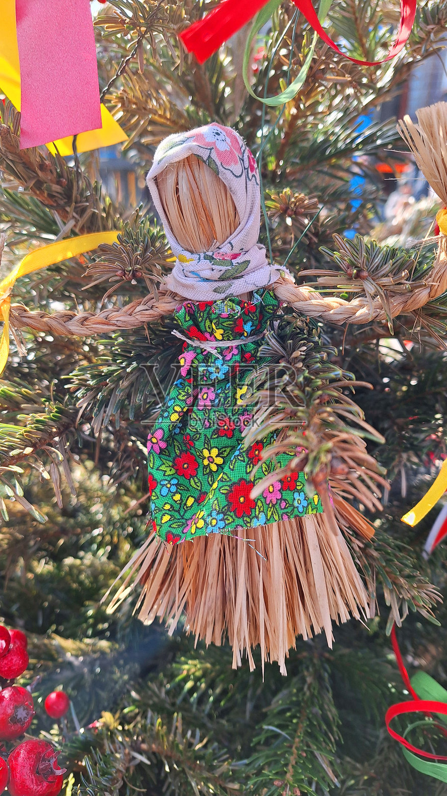 节日树上的传统稻草娃娃装饰，背景为生机勃勃的户外环境照片摄影图片