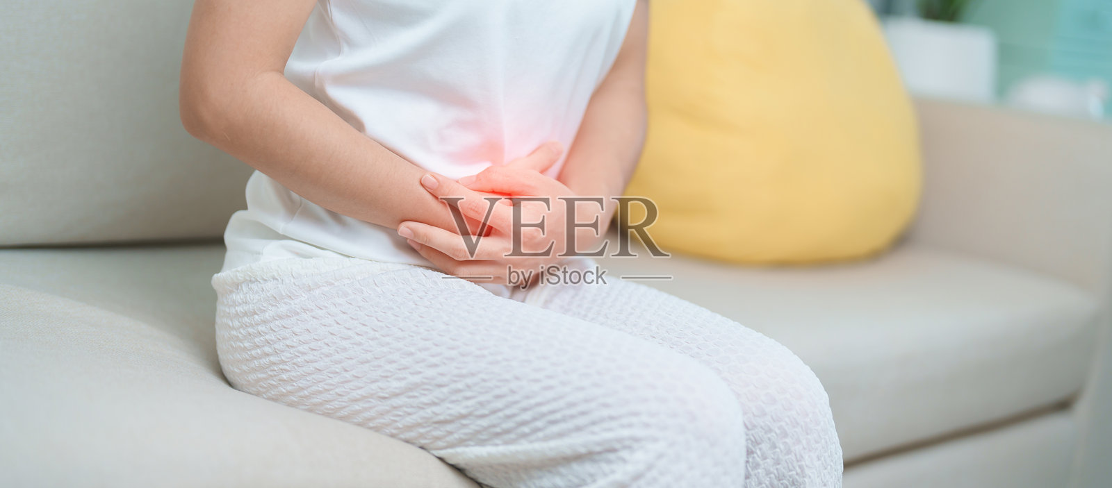 女性因食物中毒、消化不良、便秘或腹泻而感到腹部疼痛，可能与女性问题、子宫内膜异位症、子宫切除术、胃痛和月经有关，正坐在家中的沙发上。照片摄影图片