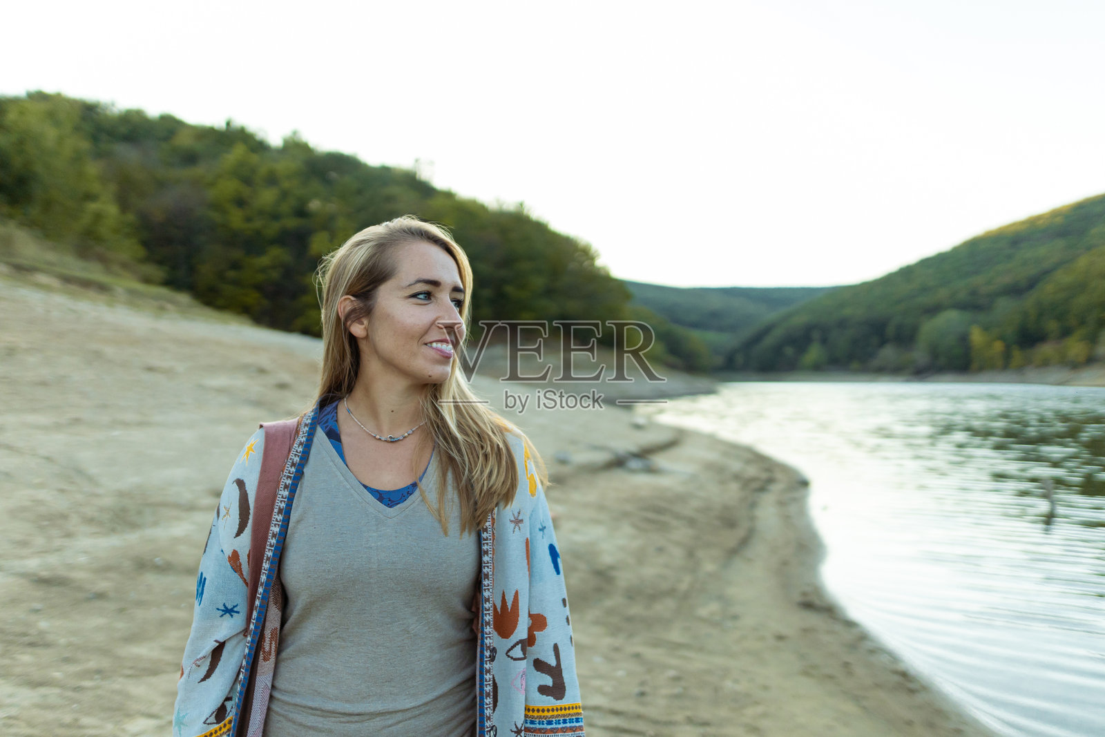 美丽的女人站在湖边，享受美丽的大自然。微笑着，探索周末时光。照片摄影图片