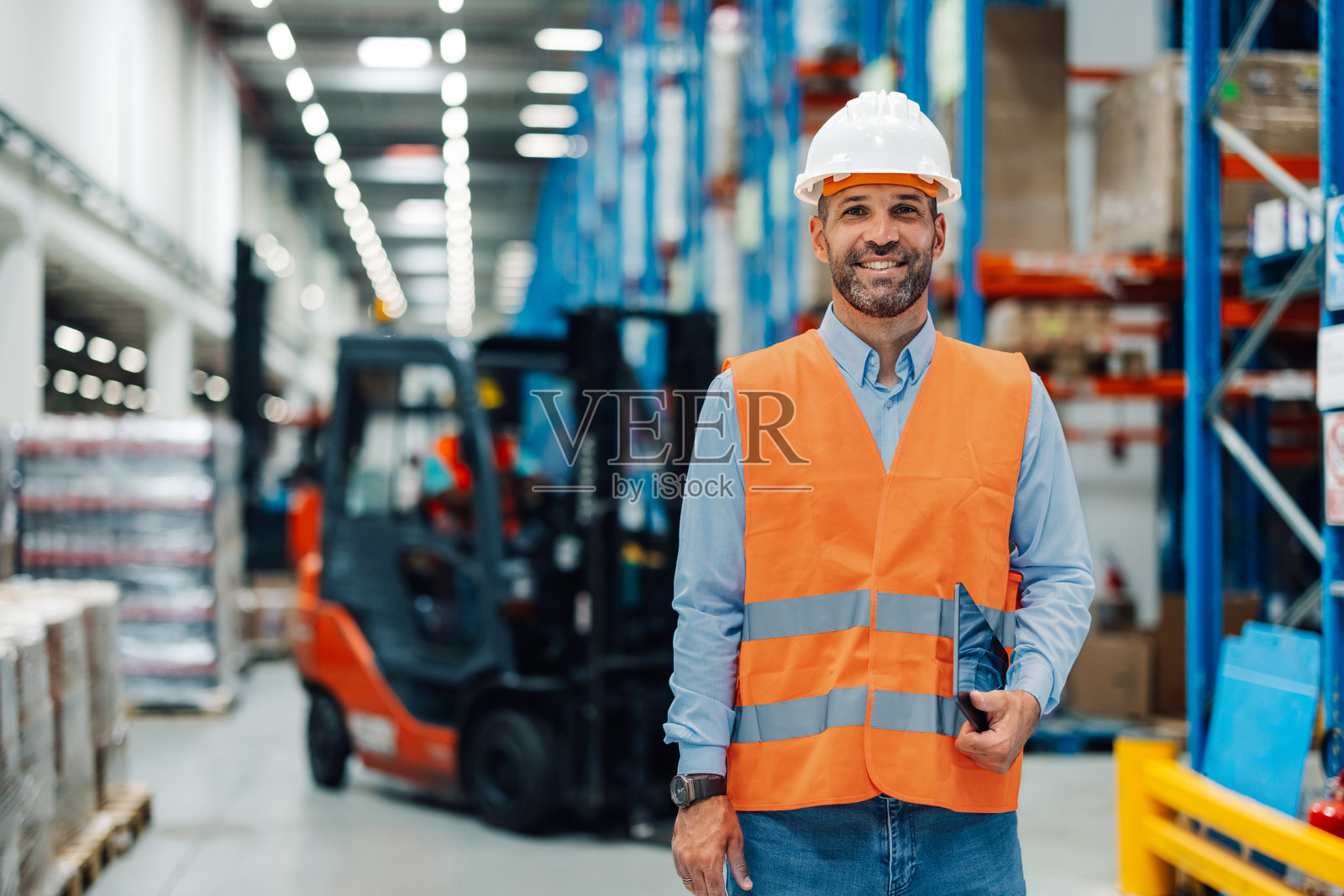 仓库工人手持数字平板，面带微笑，背景有叉车。照片摄影图片