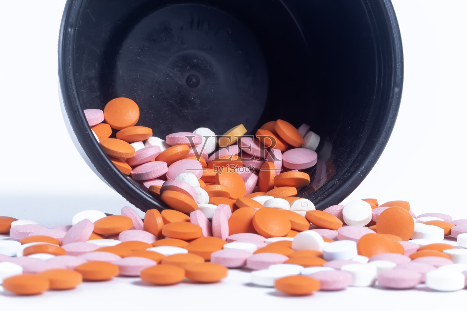 五颜六色的药丸从黑色塑料容器中洒落，背景为白色。照片摄影图片