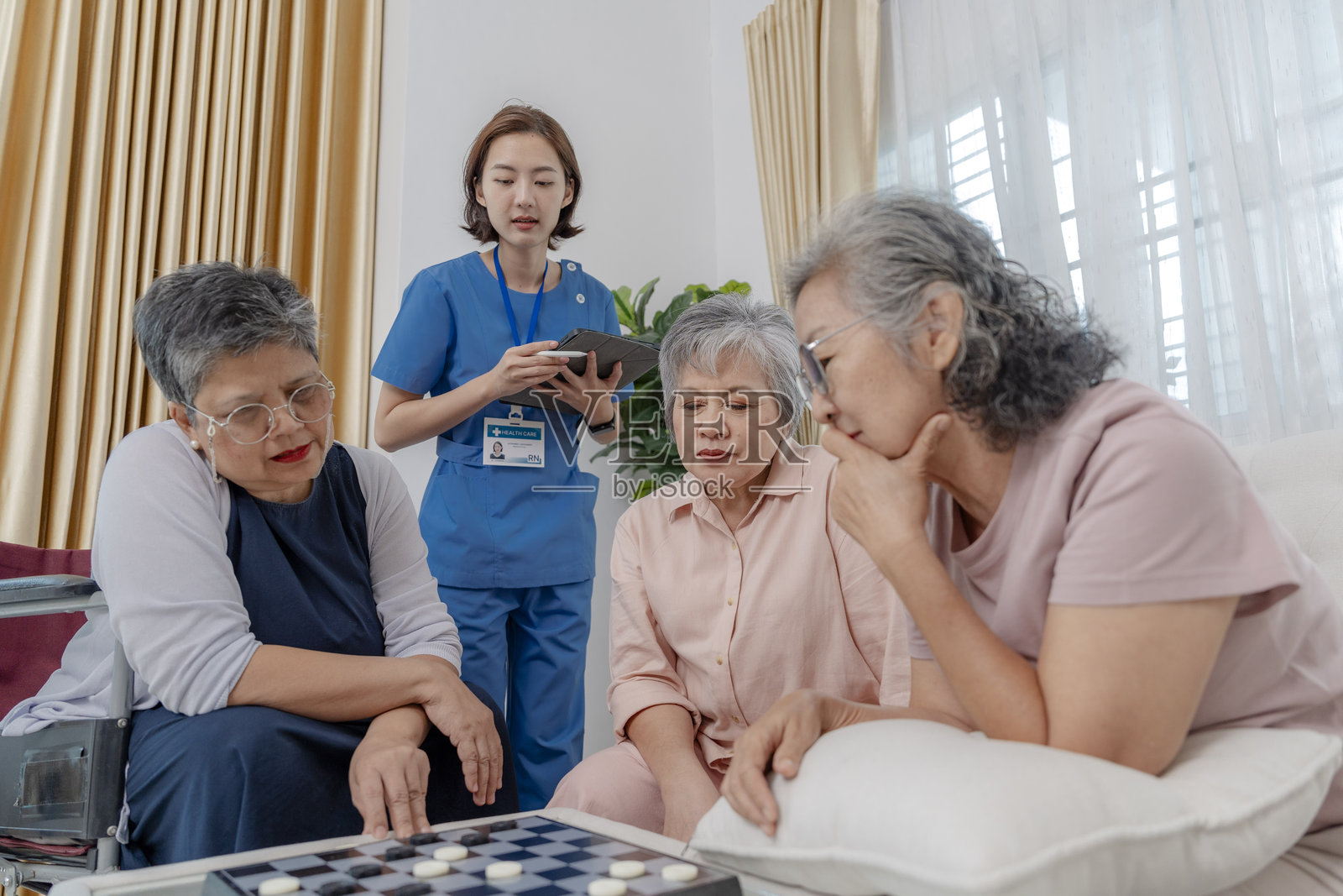 一群老年女性在玩桌游，一位医疗专业人员在平板电脑上做笔记。这个场景强调了老年人的参与、无障碍和友好的支持性护理环境。照片摄影图片