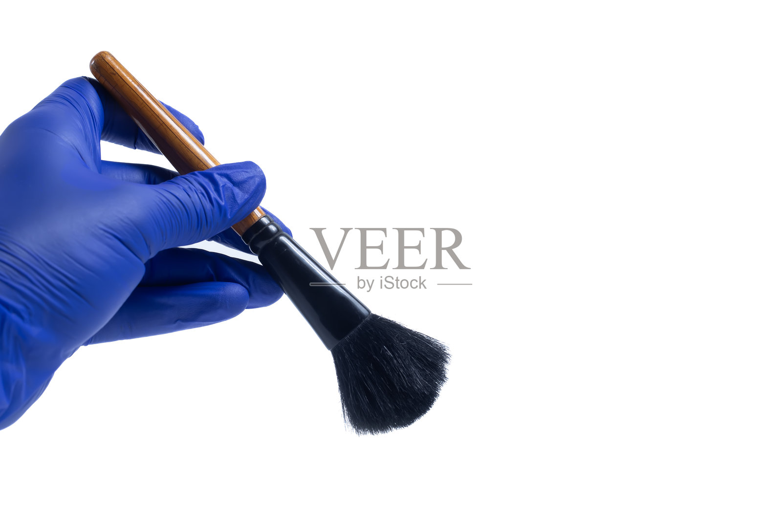戴着蓝色手套的手握着化妆刷，背景为白色。照片摄影图片