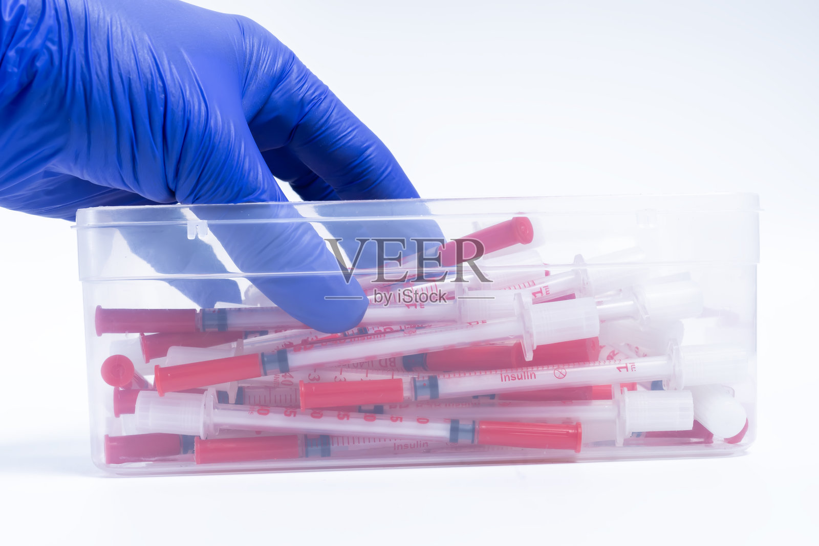 蓝色手套的医生手从白色背景上的塑料容器中取出注射器。特写镜头。照片摄影图片