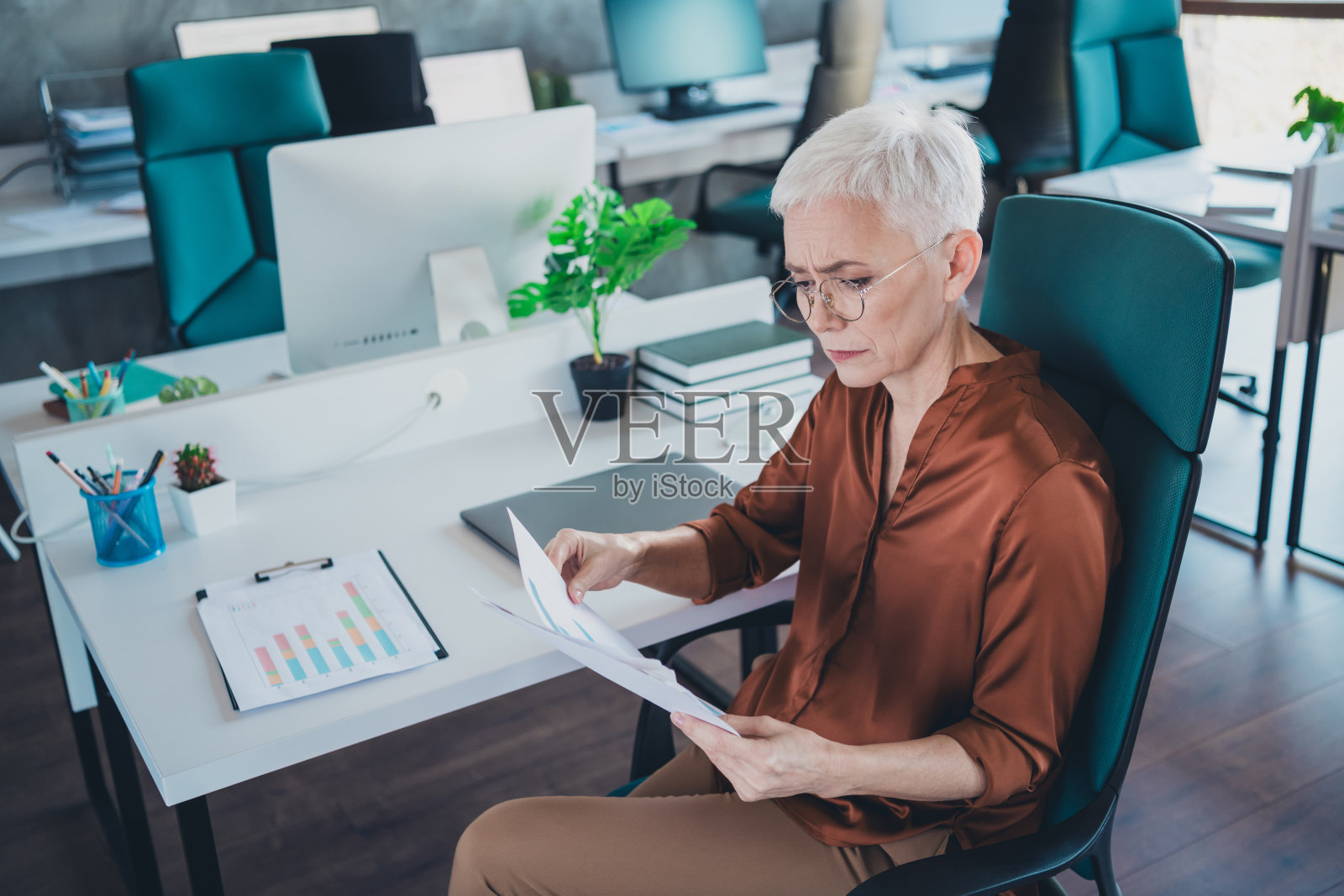 成熟的女性在办公室工作室内，穿着棕色衬衫，面露担忧，手中拿着工作文件。照片摄影图片