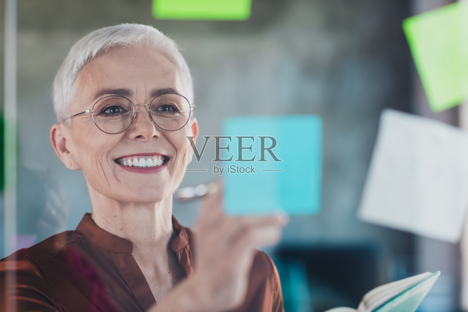 穿着棕色衬衫的高管女商人微笑着，展示贴纸创意，现代办公室内部工作空间。照片摄影图片