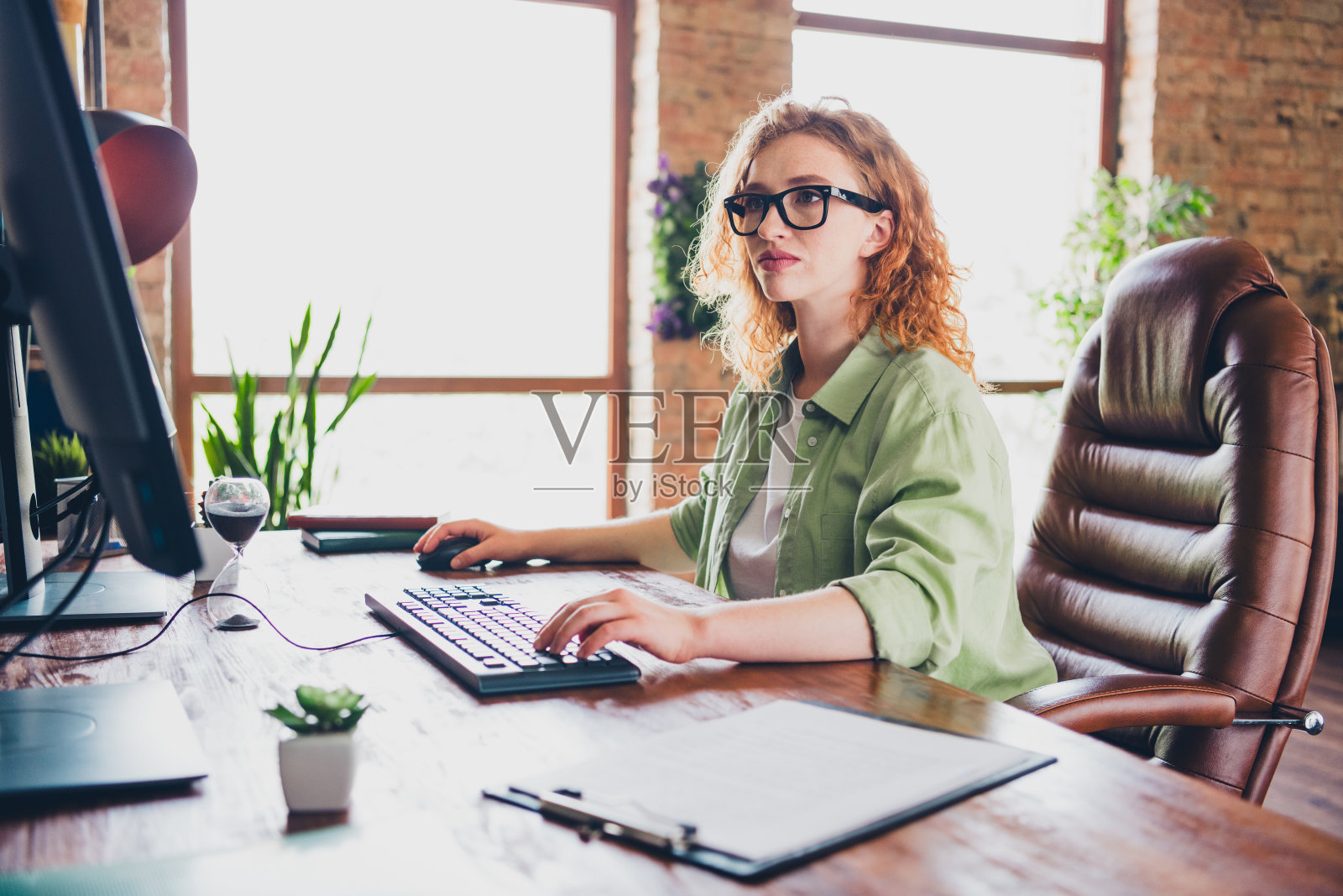 自信积极的女性招聘者穿着衬衫，戴着眼镜，在现代设备上工作，位于室内工作站的阁楼中。照片摄影图片