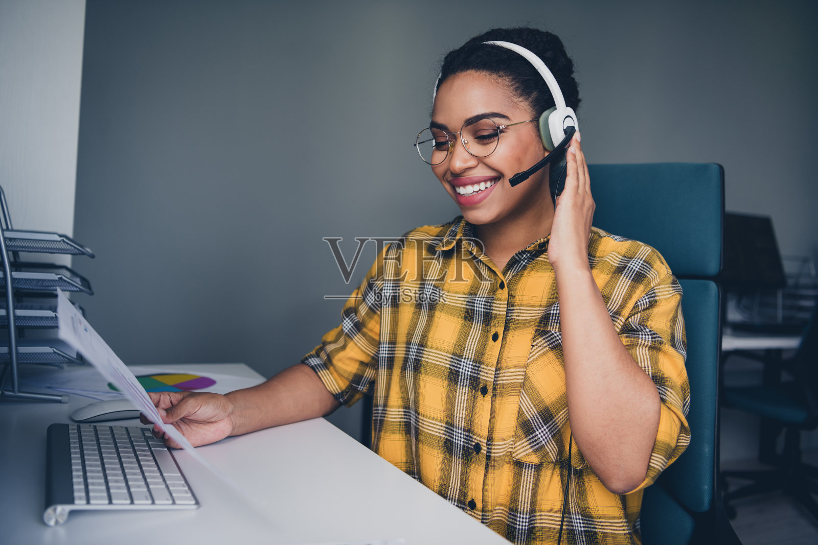 可爱的年轻女性在舒适的初创公司办公室阁楼内穿着黄色格子衬衫阅读文件，作为呼叫中心的工作人员。照片摄影图片