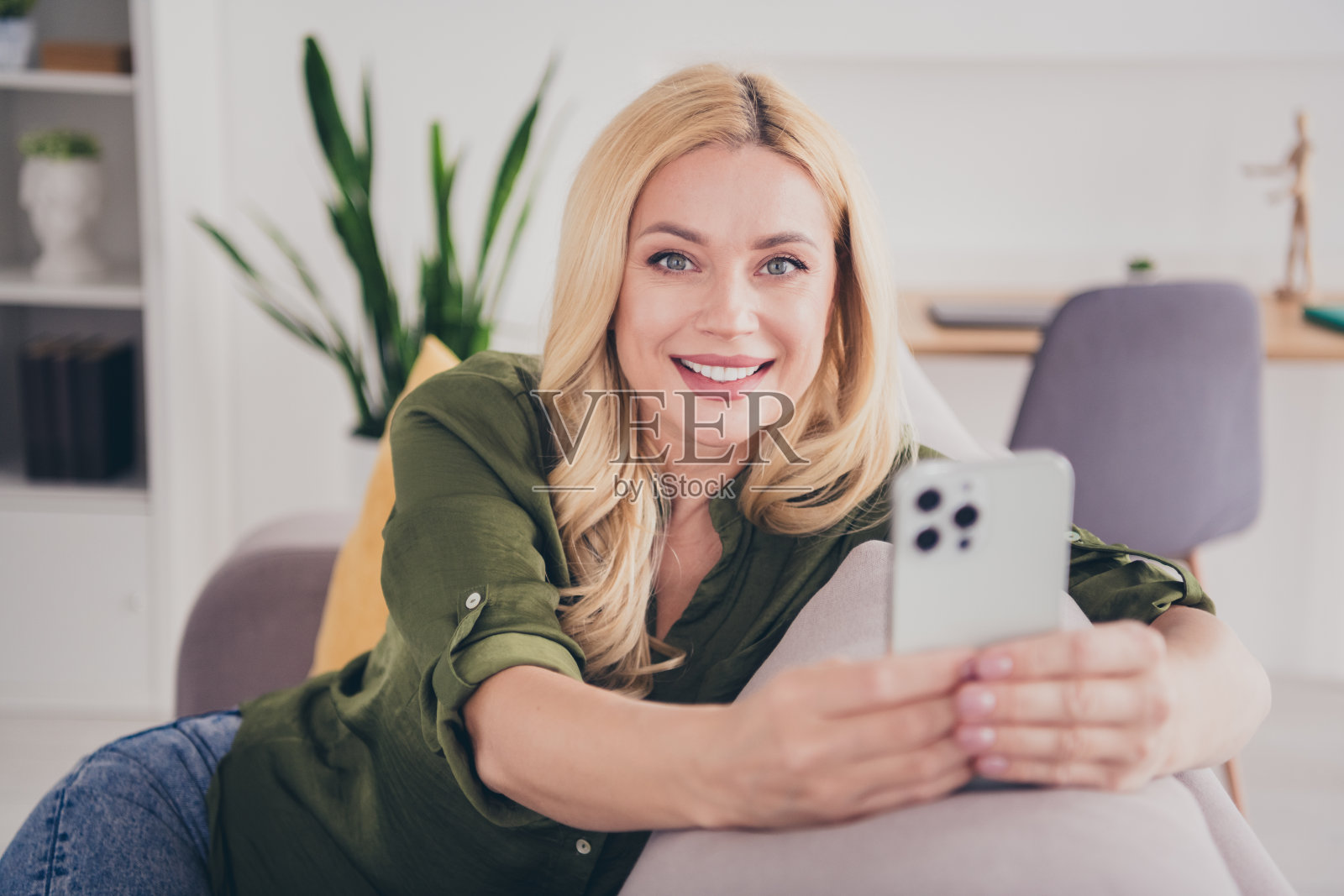 可爱的女性穿着时尚的衣服，坐在沙发上，手持手机阅读社交媒体，室内客厅环境。照片摄影图片