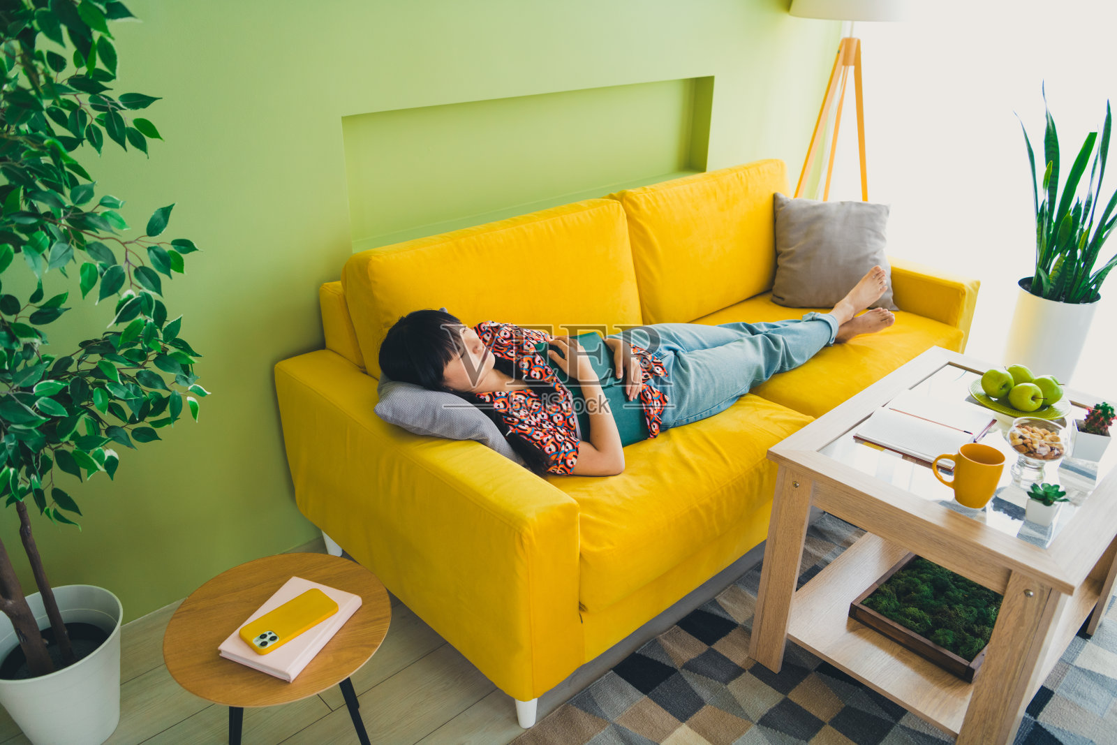 年轻漂亮的女子在现代公寓的沙发上睡觉，手中抱着一本书，享受周末时光。照片摄影图片